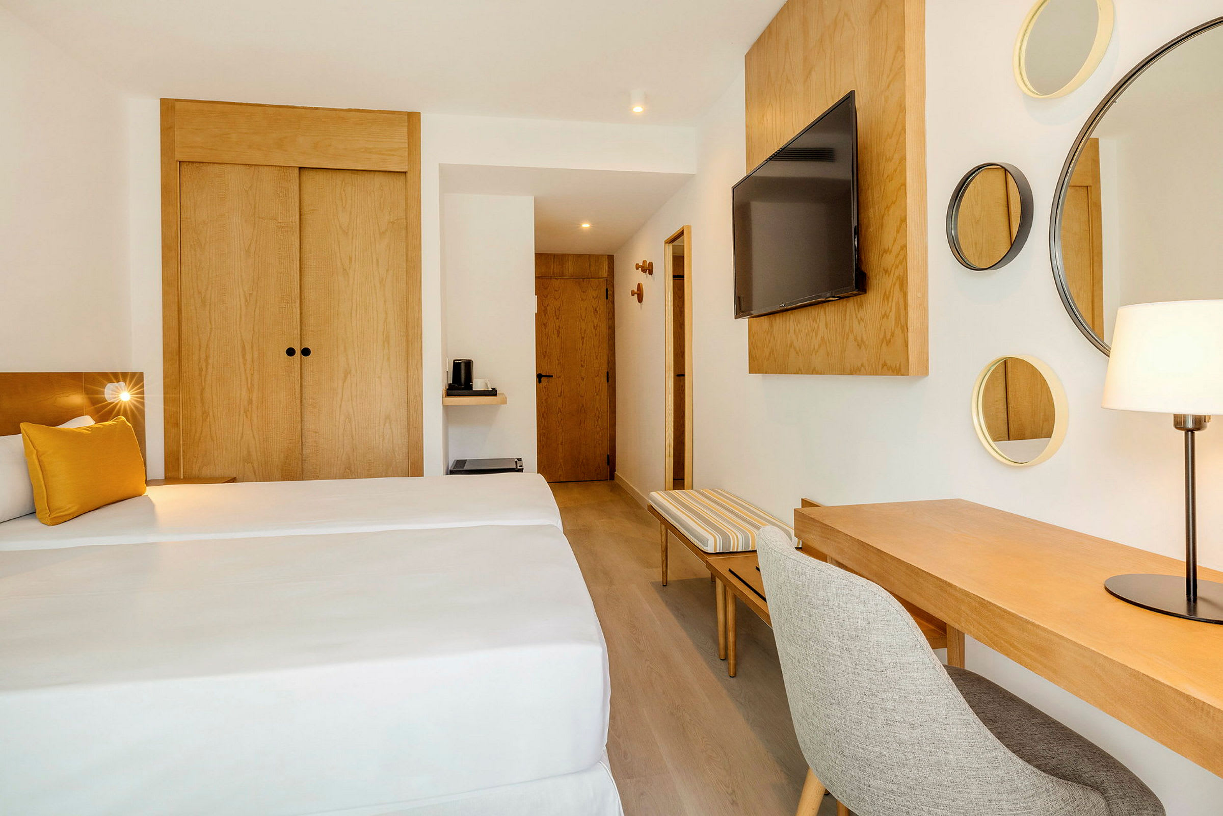 Ett hotellrum med två enkelsängar, ett skrivbord med stol, en väggmonterad TV och trämöbler. (AI-genererad text)