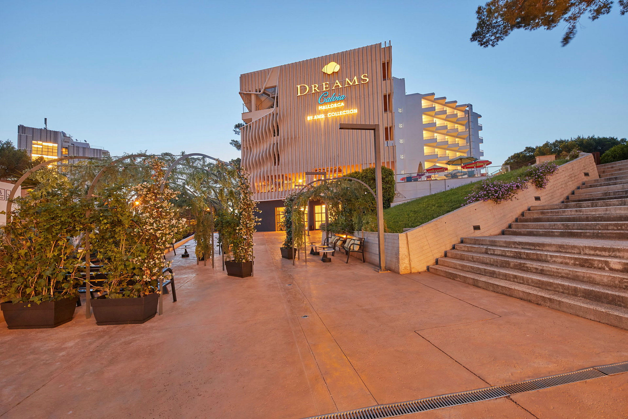 En byggnad med skylt som lyser "Dreams Calvia Mallorca" med en trädgårdsmiljö och trappsteg i förgrunden. (AI-genererad text)