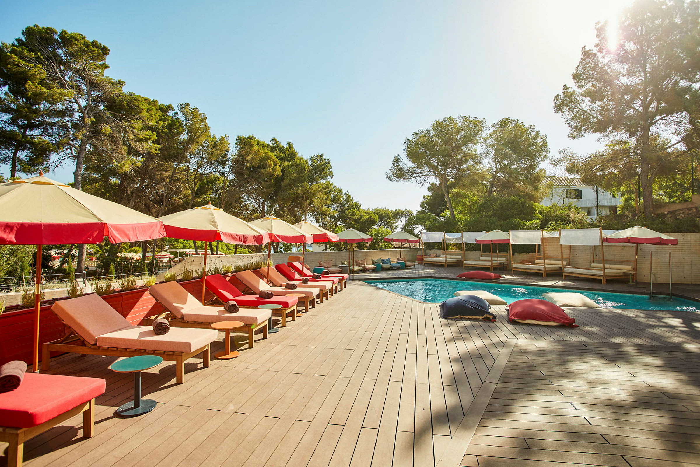 En solterrass med solstolar och parasoller bredvid en pool, omgiven av grönska. (AI-genererad text)