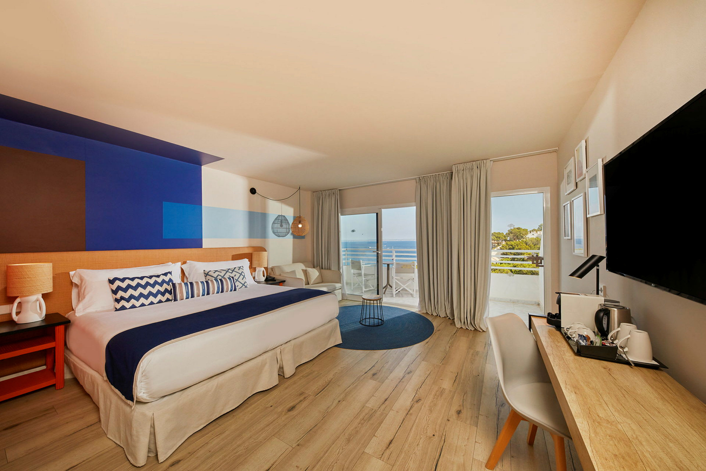 Ett hotellrum med stor säng, skrivbord och utsikt över havet från balkong. (AI-genererad text)