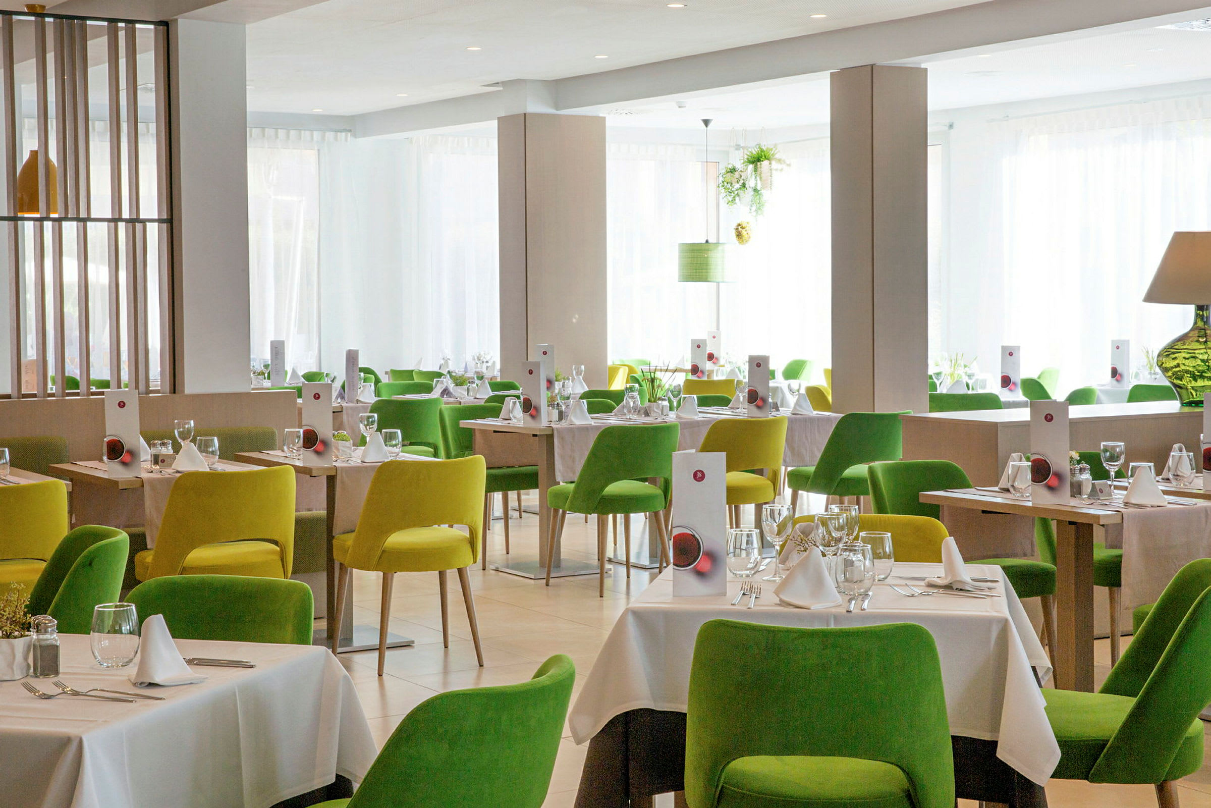 Ett ljust och modernt restaurangområde med gröna och gula stolar och dukade bord. (AI-genererad text)