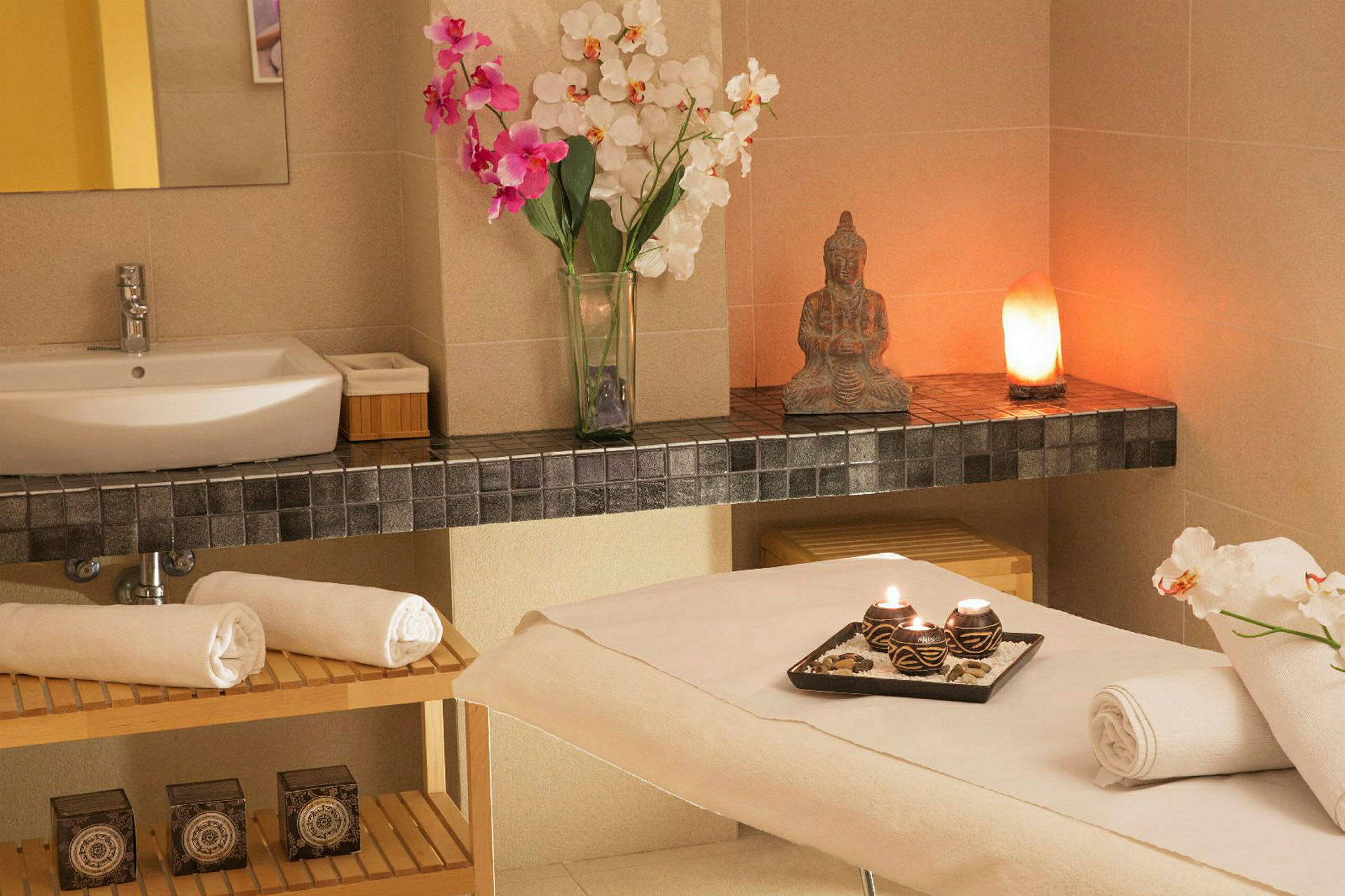 Ett välkomnande spa-rum med massagebänk, handdukar och en bricka med tända ljus samt en tvättställskommod. (AI-genererad text)