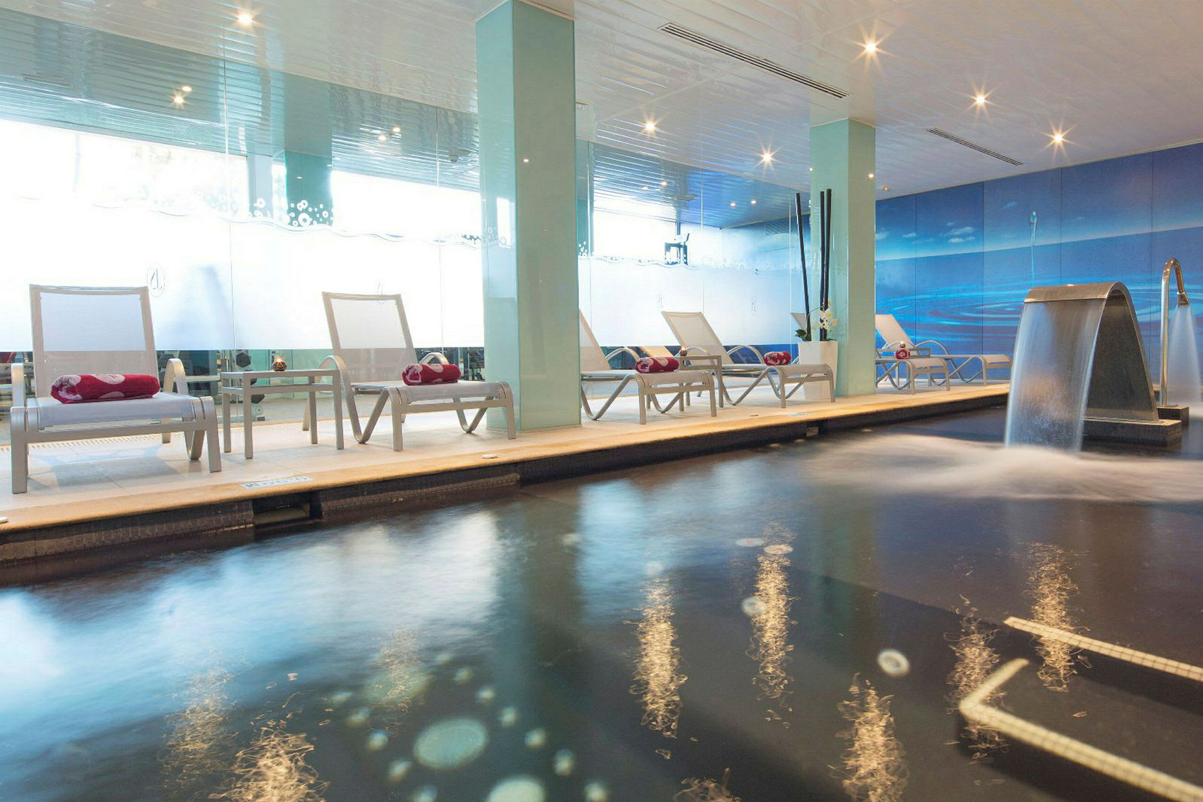 Inomhuspool med solstolar och vattenfall. (AI-genererad text)