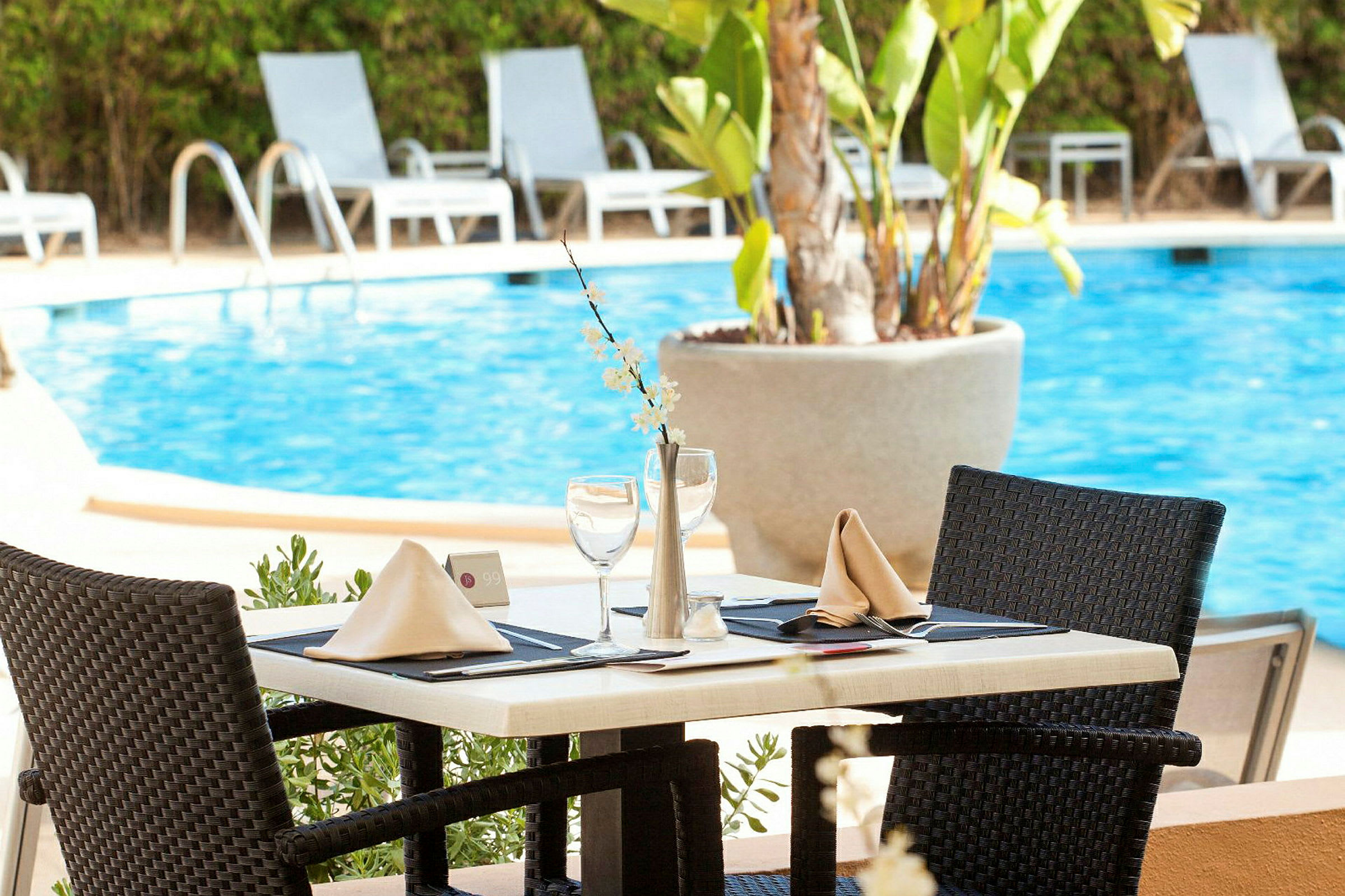 Ett dukat bord vid en pool, omgiven av solstolar. (AI-genererad text)