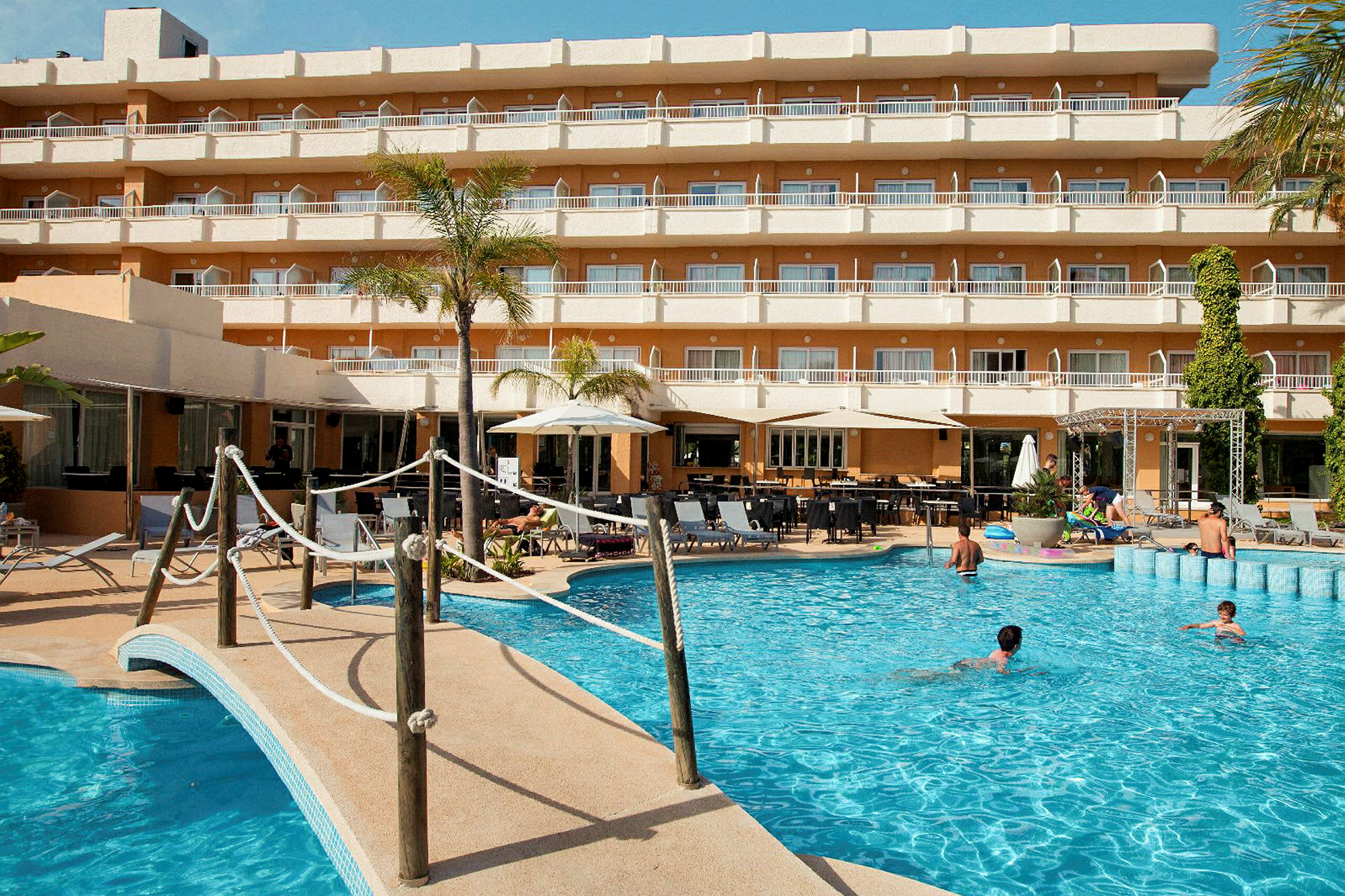 En utomhuspool framför ett hotell med flera våningar och balkonger. (AI-genererad text)