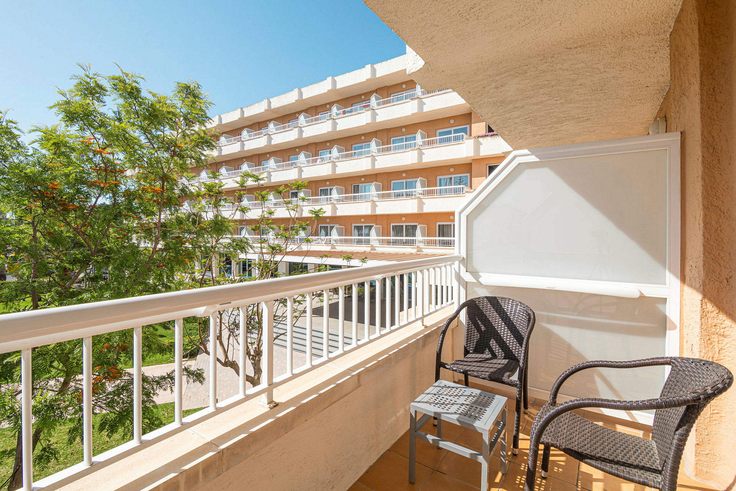 Balkong med två korgstolar och ett litet bord vid ett hotell. (AI-genererad text)