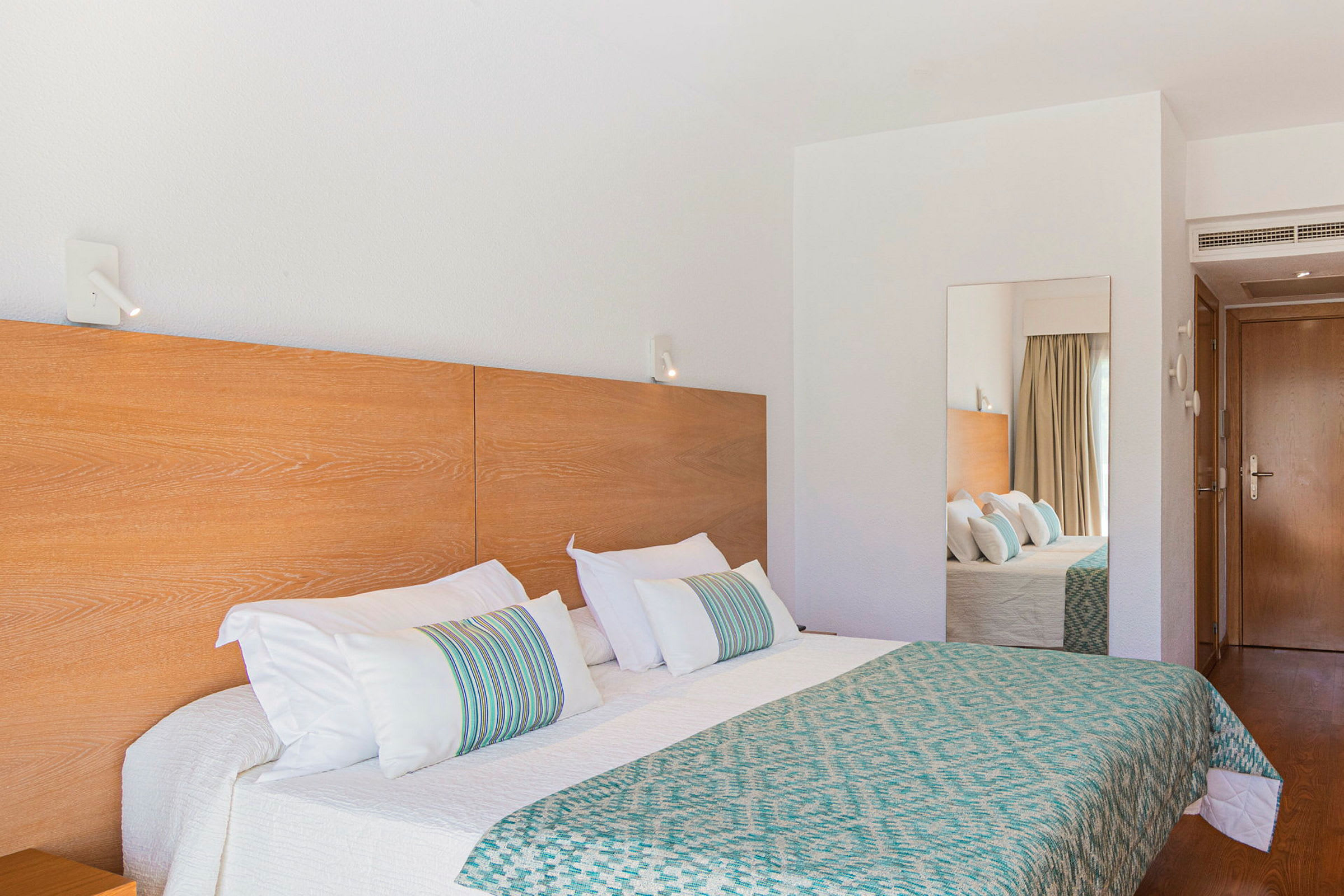 En hotellrum med dubbelsäng, sängbord och spegel på väggen. (AI-genererad text)