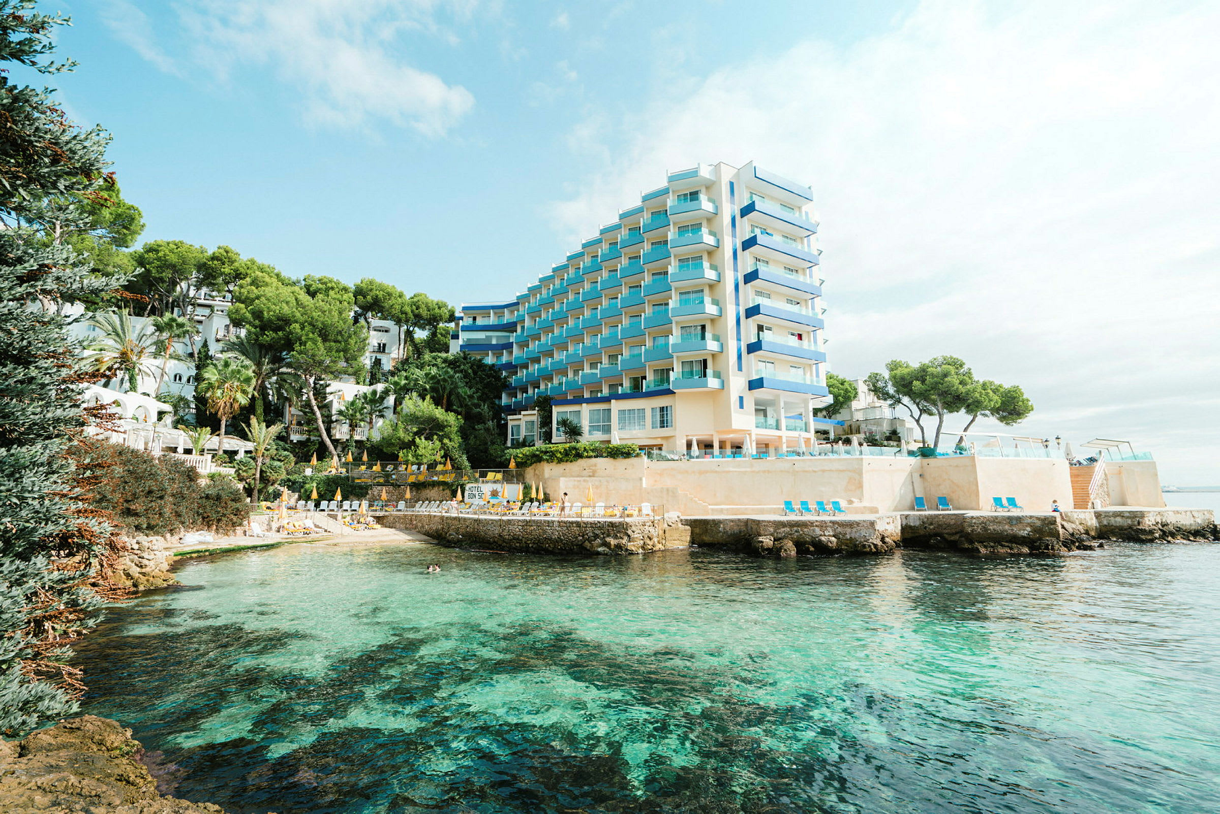 Bild av ett hotellkomplex vid en klar, turkos havsvik omgiven av grönska. (AI-genererad text)