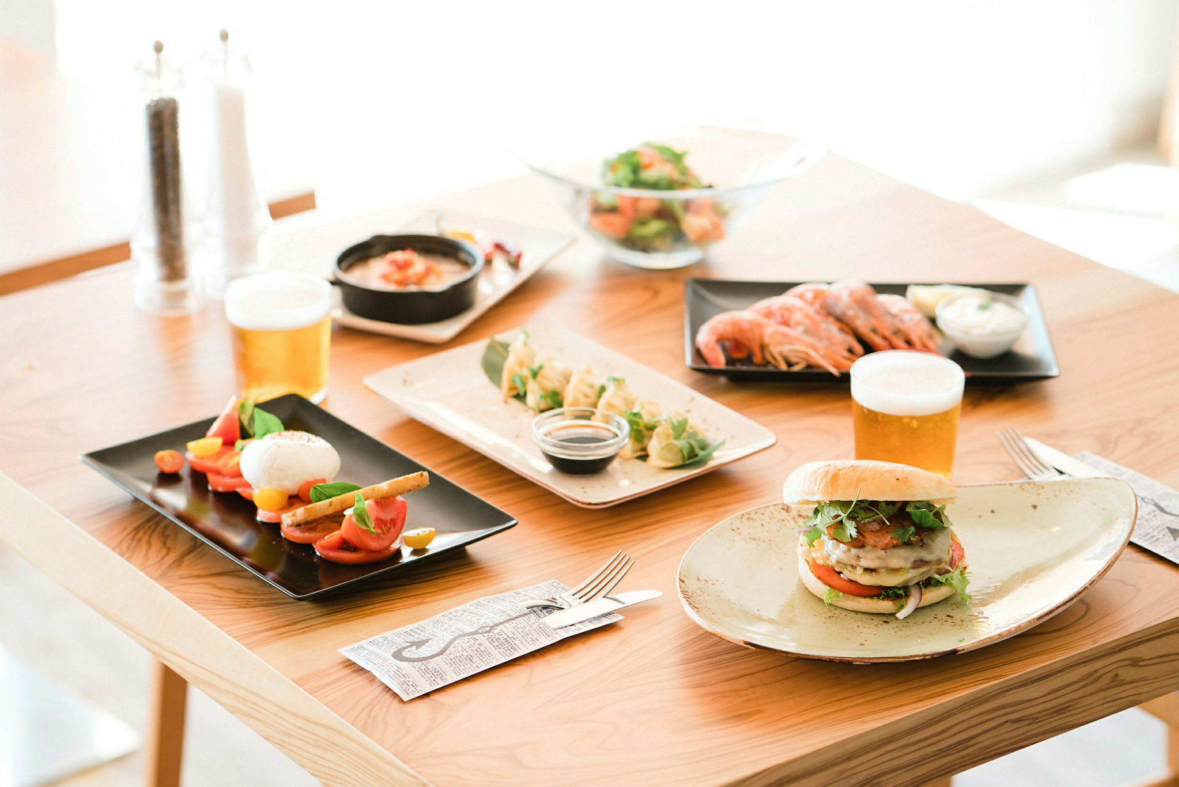 Ett bord med olika maträtter och drycker, inklusive sallad, räkor, burgare och öl. (AI-genererad text)