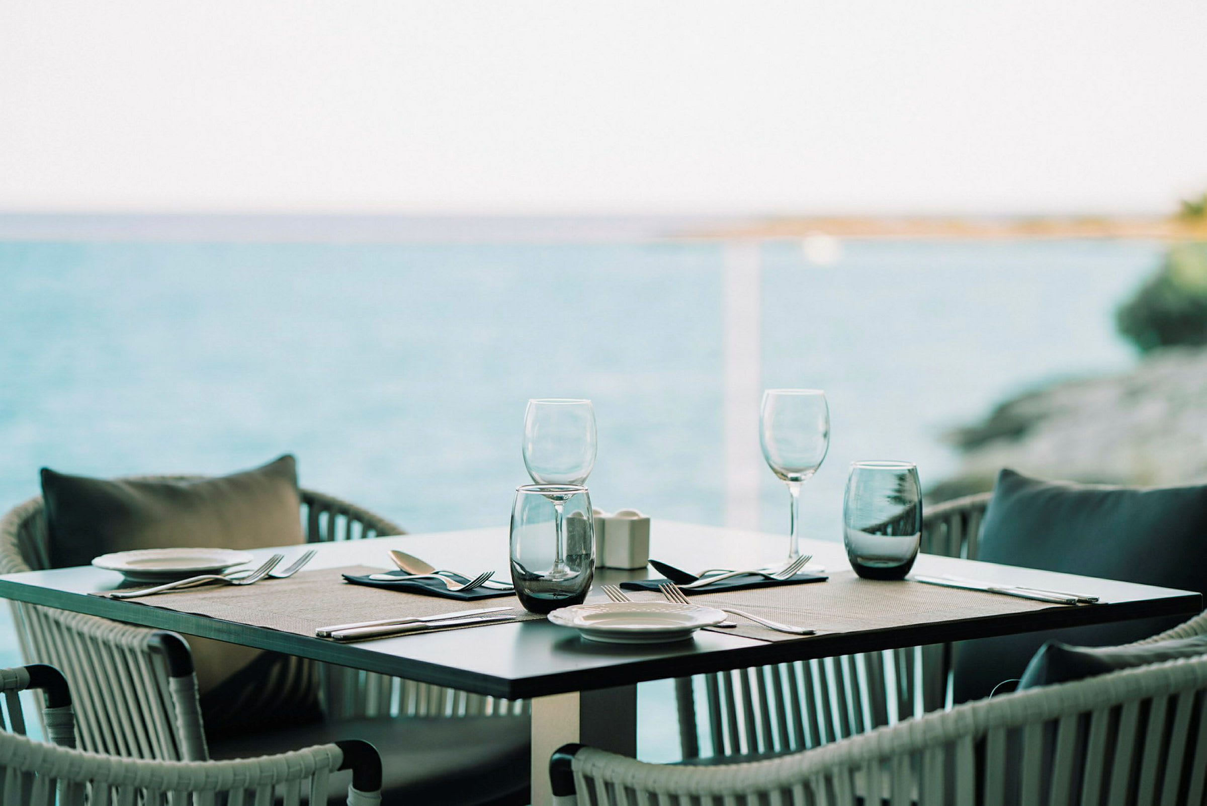 Ett dukat bord med glas och bestick vid havet. (AI-genererad text)