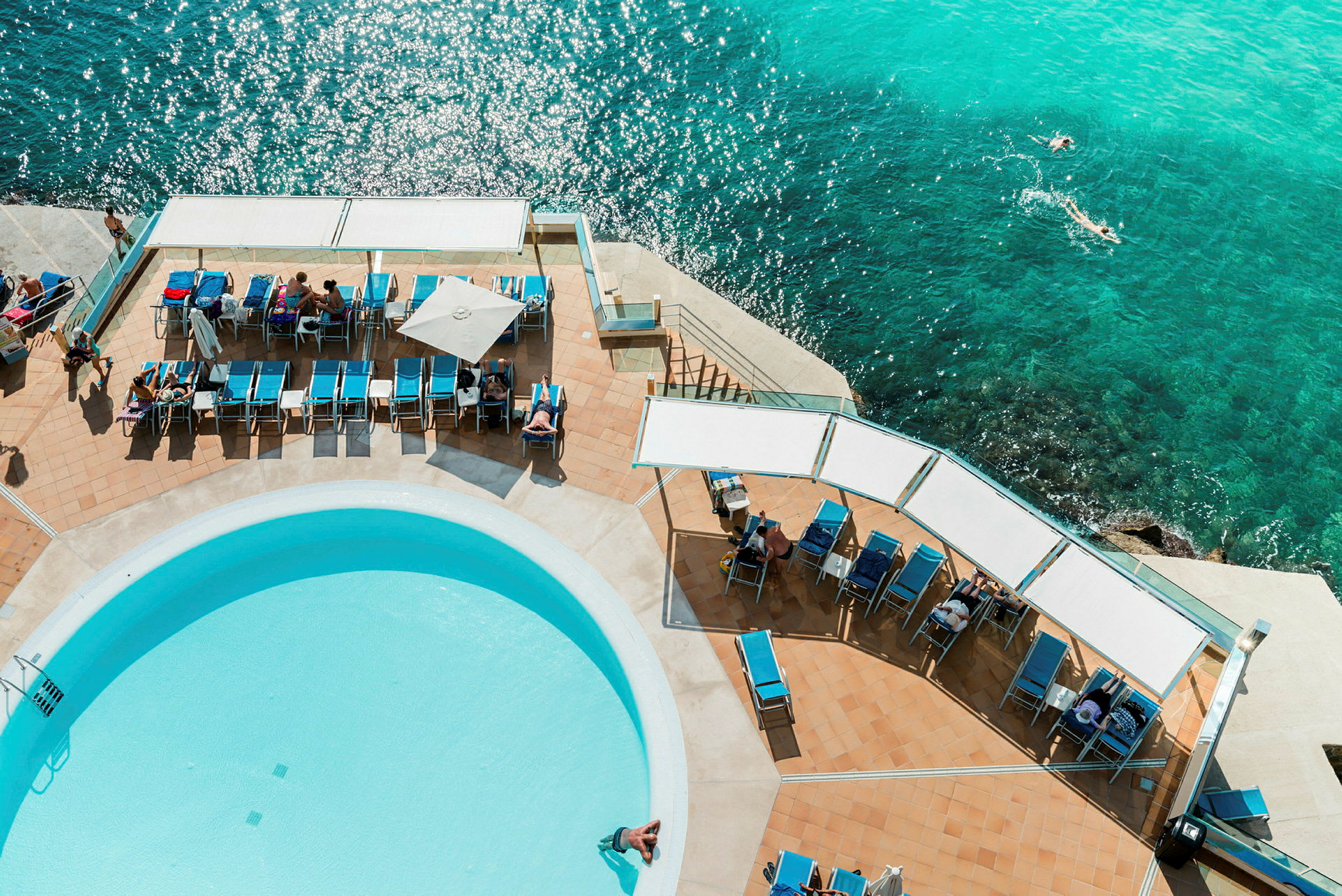 Solstolar och en pool vid havet sett från ovan. (AI-genererad text)