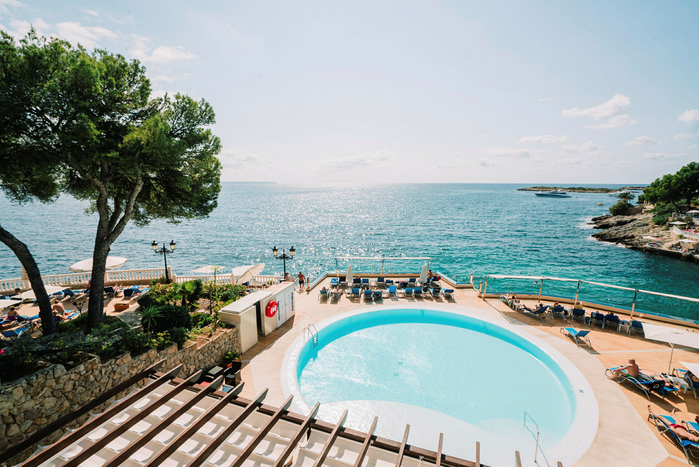 Utsikt över en soliga pool och terrass med solstolar, med havet i bakgrunden. (AI-genererad text)