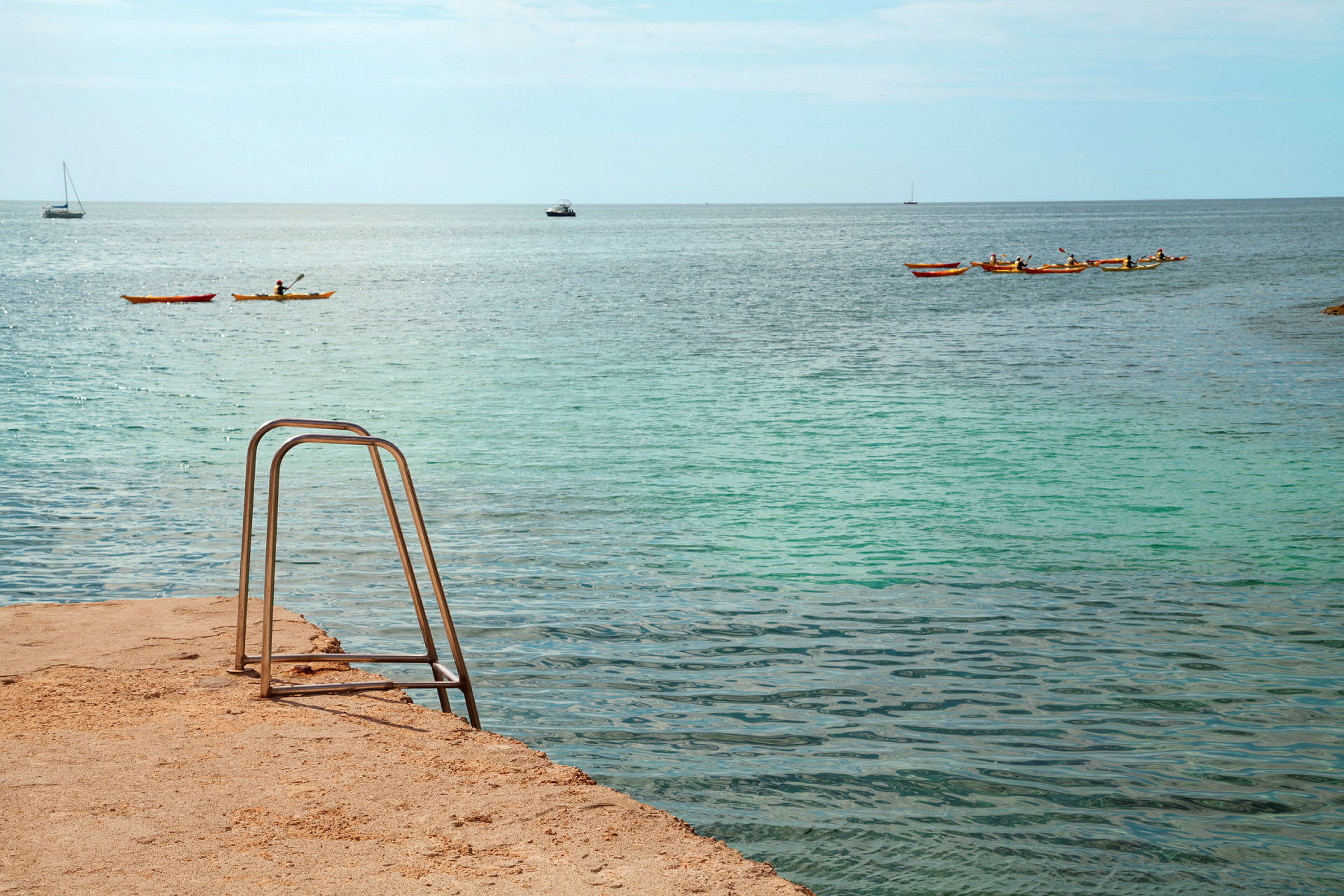 En badstege vid havet, med kajaker och båtar på vattnet. (AI-genererad text)