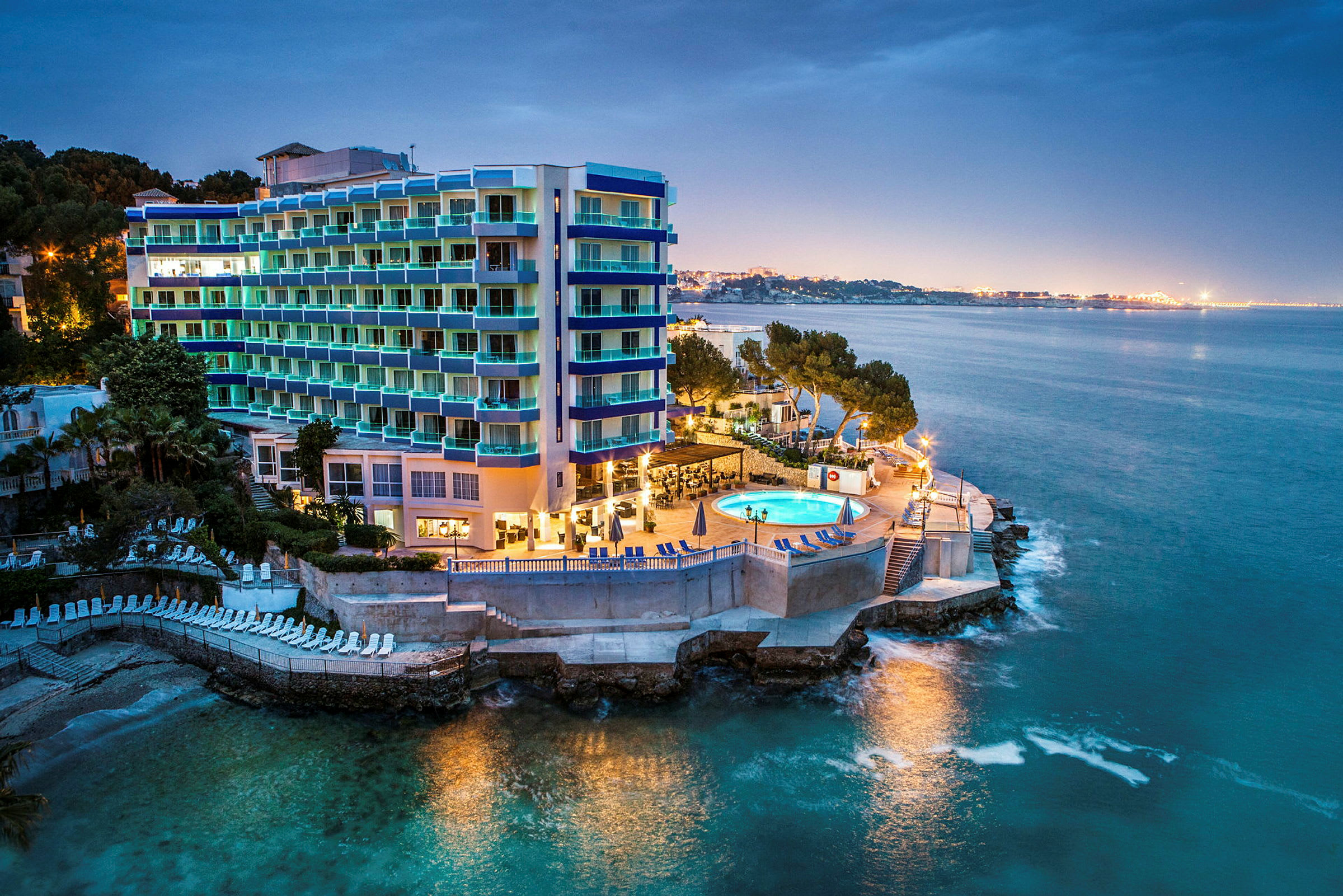 Bild av ett hotell vid havet med en upplyst pool och omgivande byggnader. (AI-genererad text)