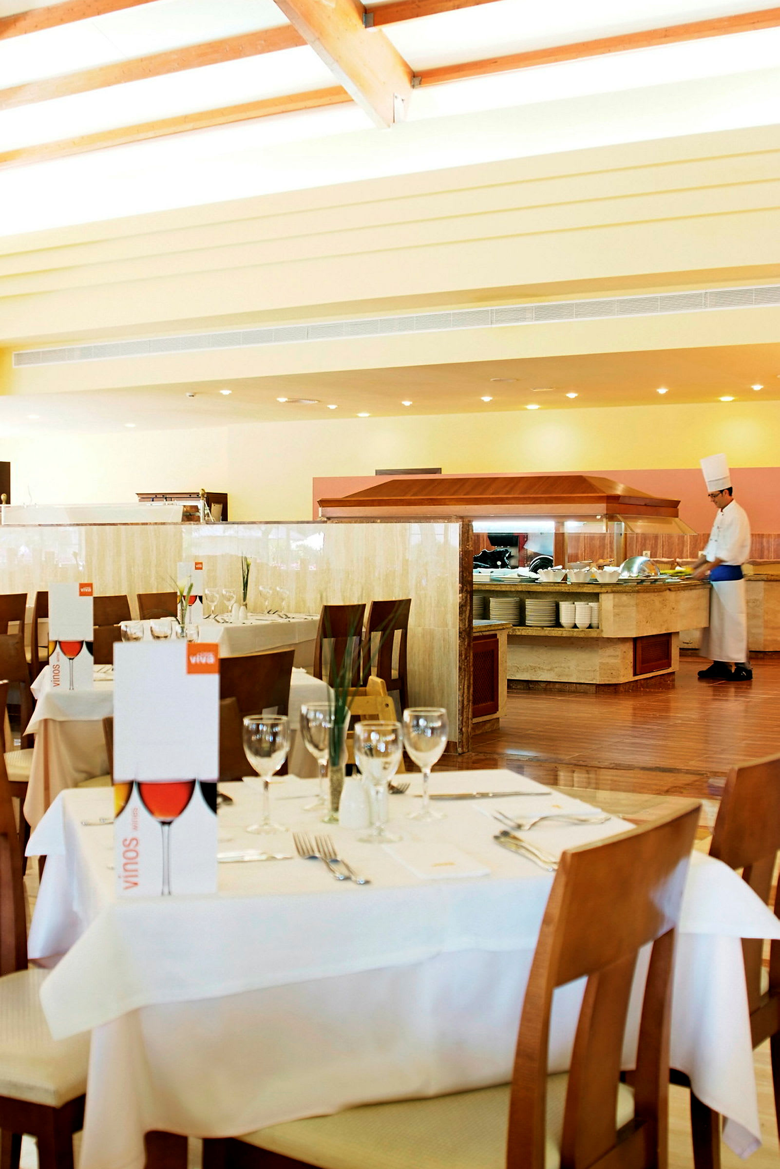 En restaurang med dukade bord och en bufféstation där en kock arbetar. (AI-genererad text)