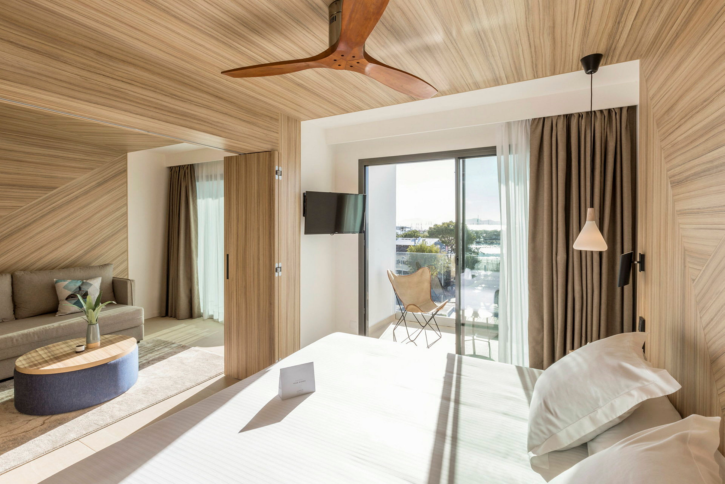 Ett hotellrum med modern inredning, säng, soffa, och en balkong med glasdörrar. (AI-genererad text)