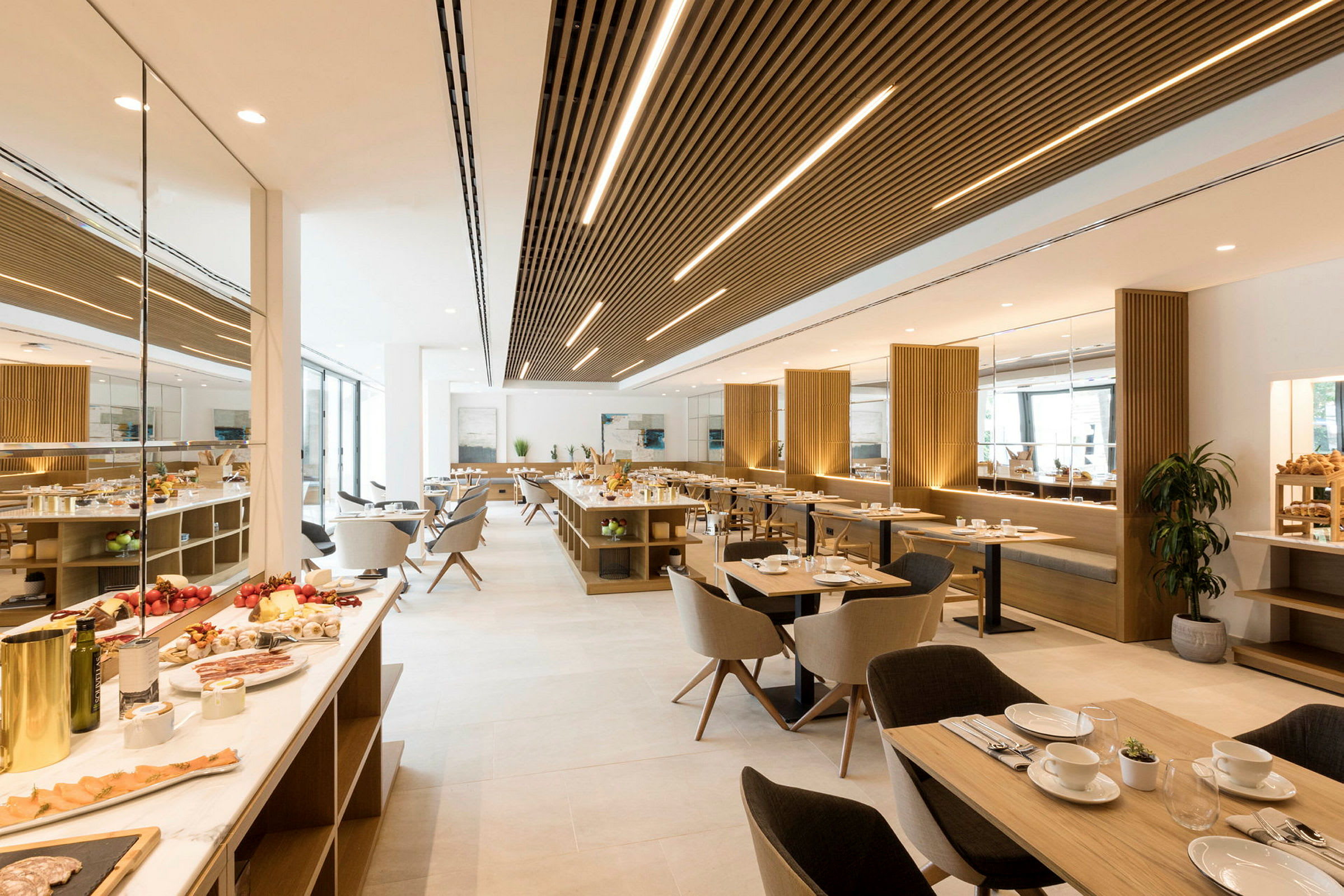 En modern restaurang med ljus inredning som visar matbord, matstolar och serveringsbord. Tallrikar och glas står klara för servering, och färsk mat är uppdukad. (AI-genererad text)