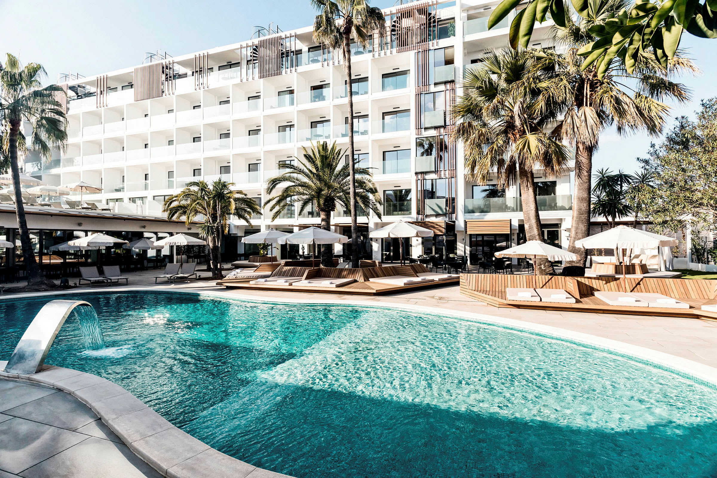 Bild av ett hotell med en swimmingpool, solstolar och parasoller, omgivet av palmer. (AI-genererad text)