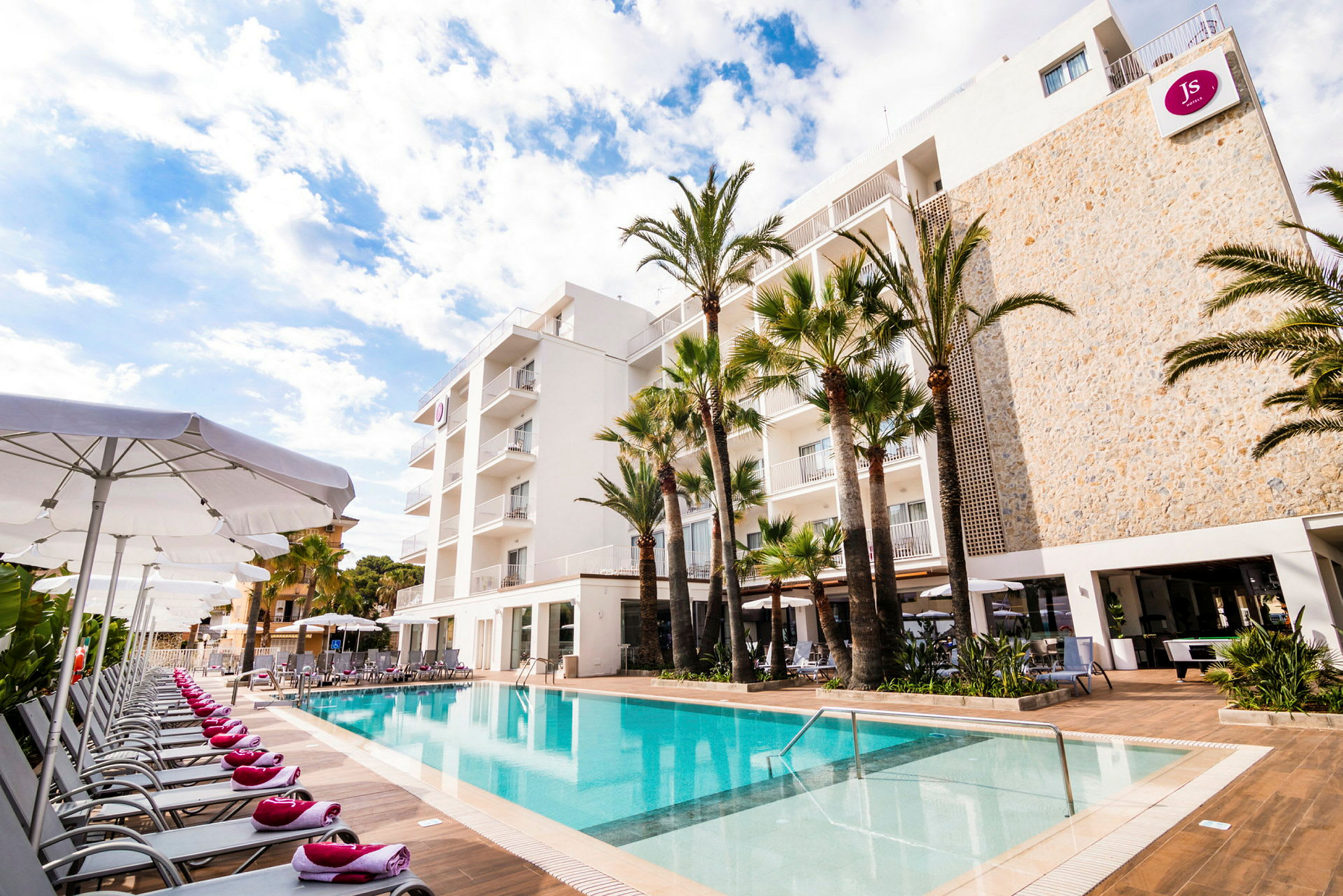 Utomhuspool med solstolar och ett hotell i bakgrunden. (AI-genererad text)