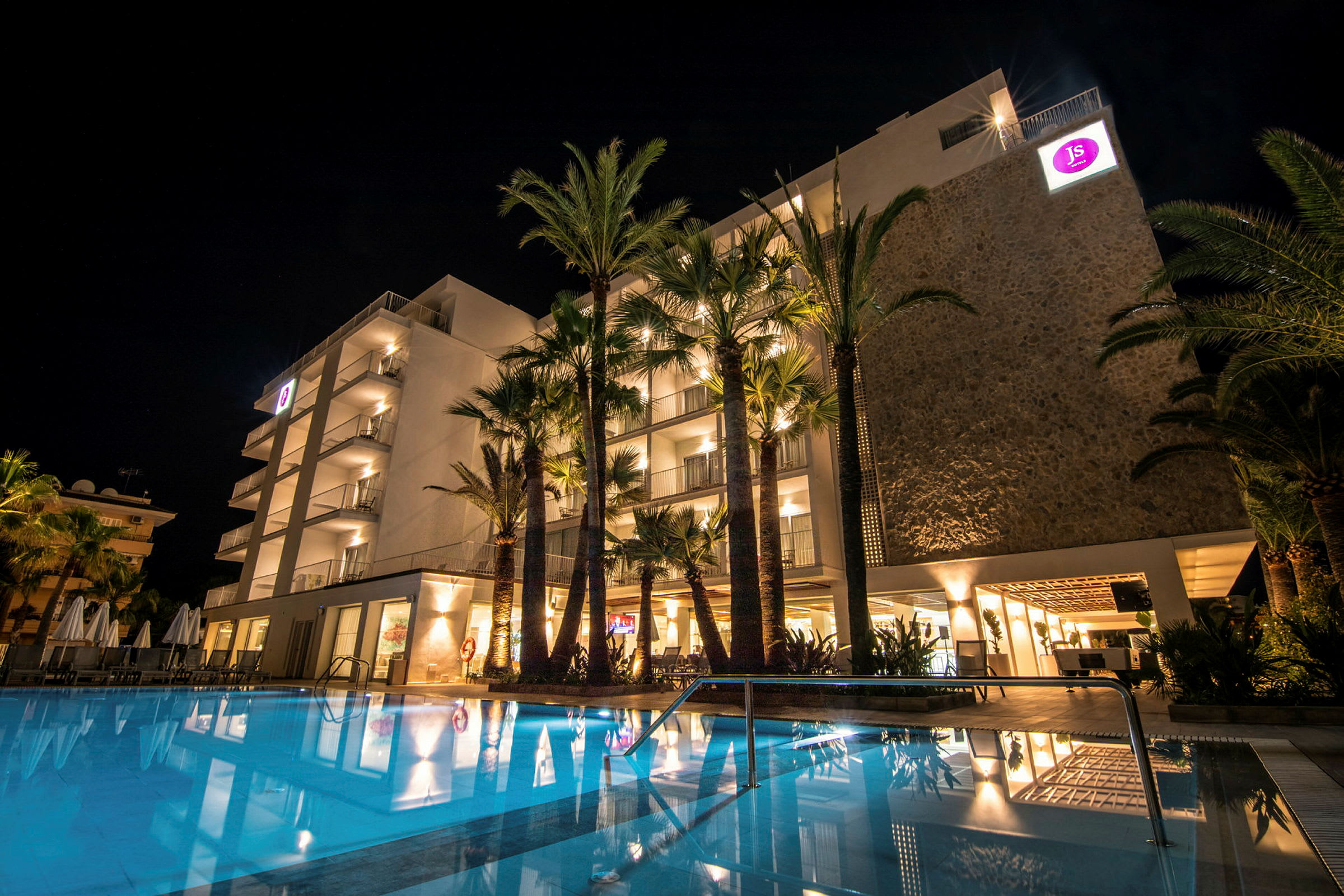 Hotellbyggnad med upplyst fasad och en pool på kvällen. (AI-genererad text)