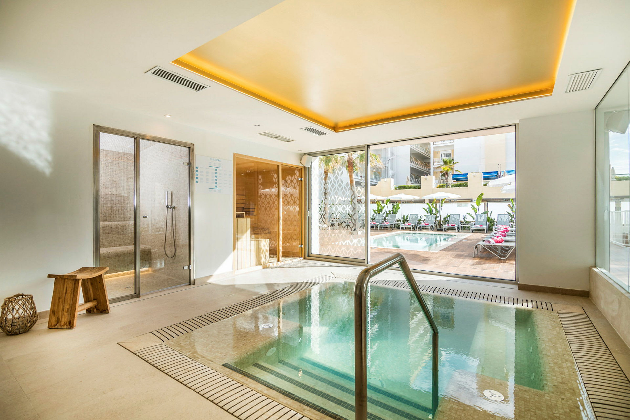 Bild av ett inomhus spa med en varm pool och utsikt över en utomhuspool genom stora fönster. (AI-genererad text)