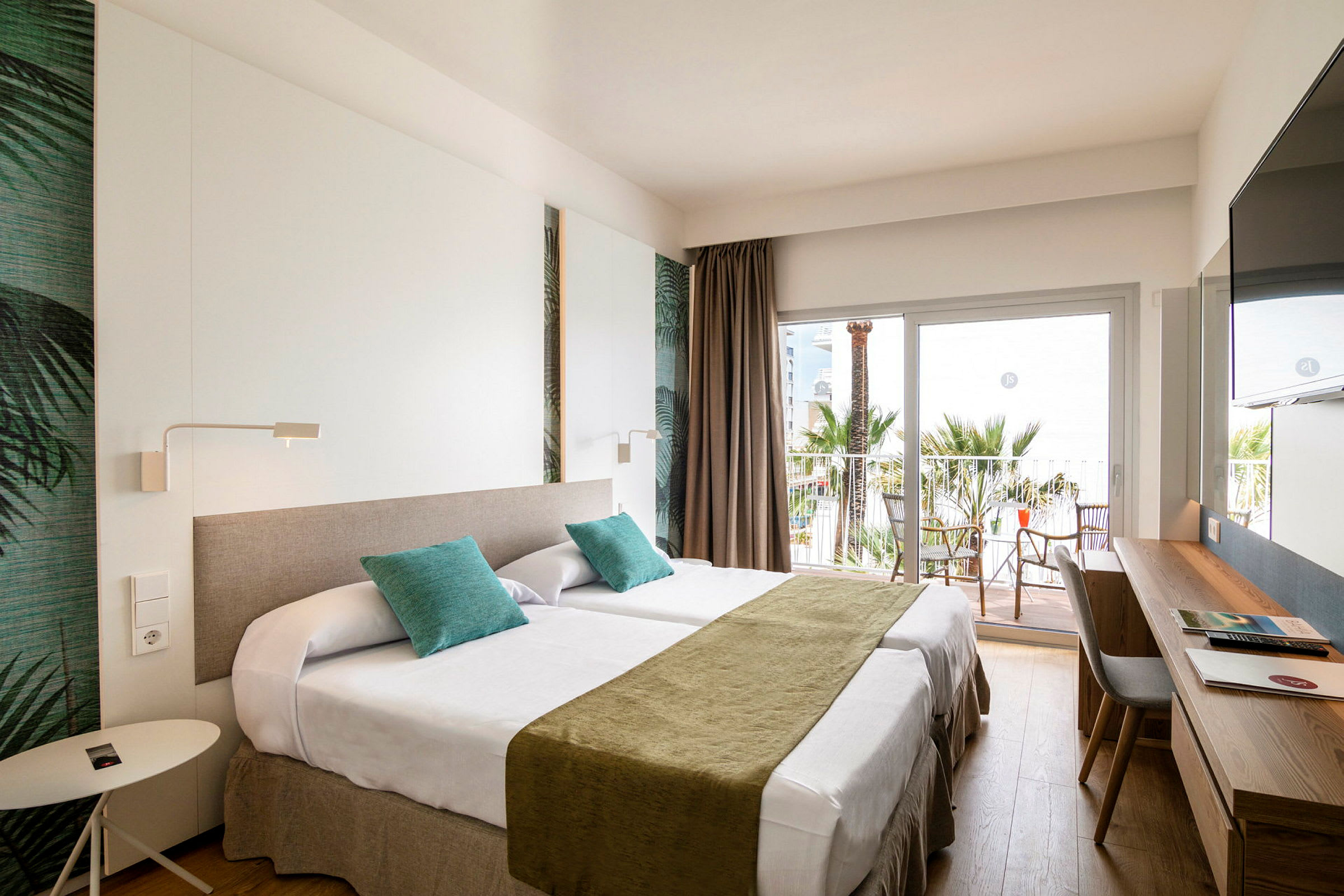 Hotellrum med två enkelsängar, skrivbord och balkong med utsikt mot palmer. (AI-genererad text)