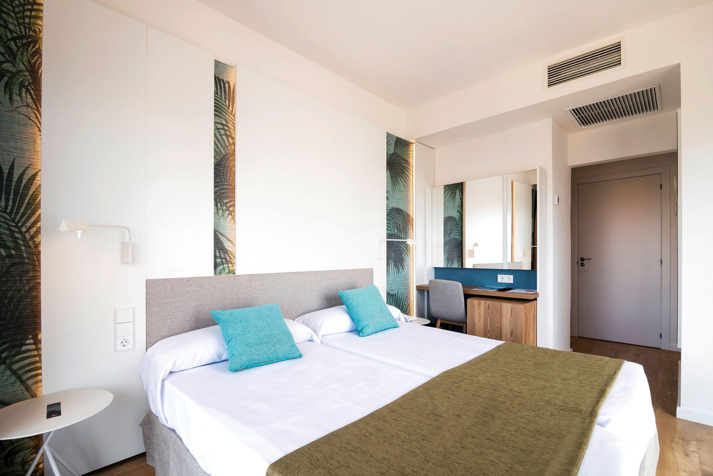 Ett hotellrum med två sängar dekorerade med turkosa kuddar och en grön sängfilt. (AI-genererad text)
