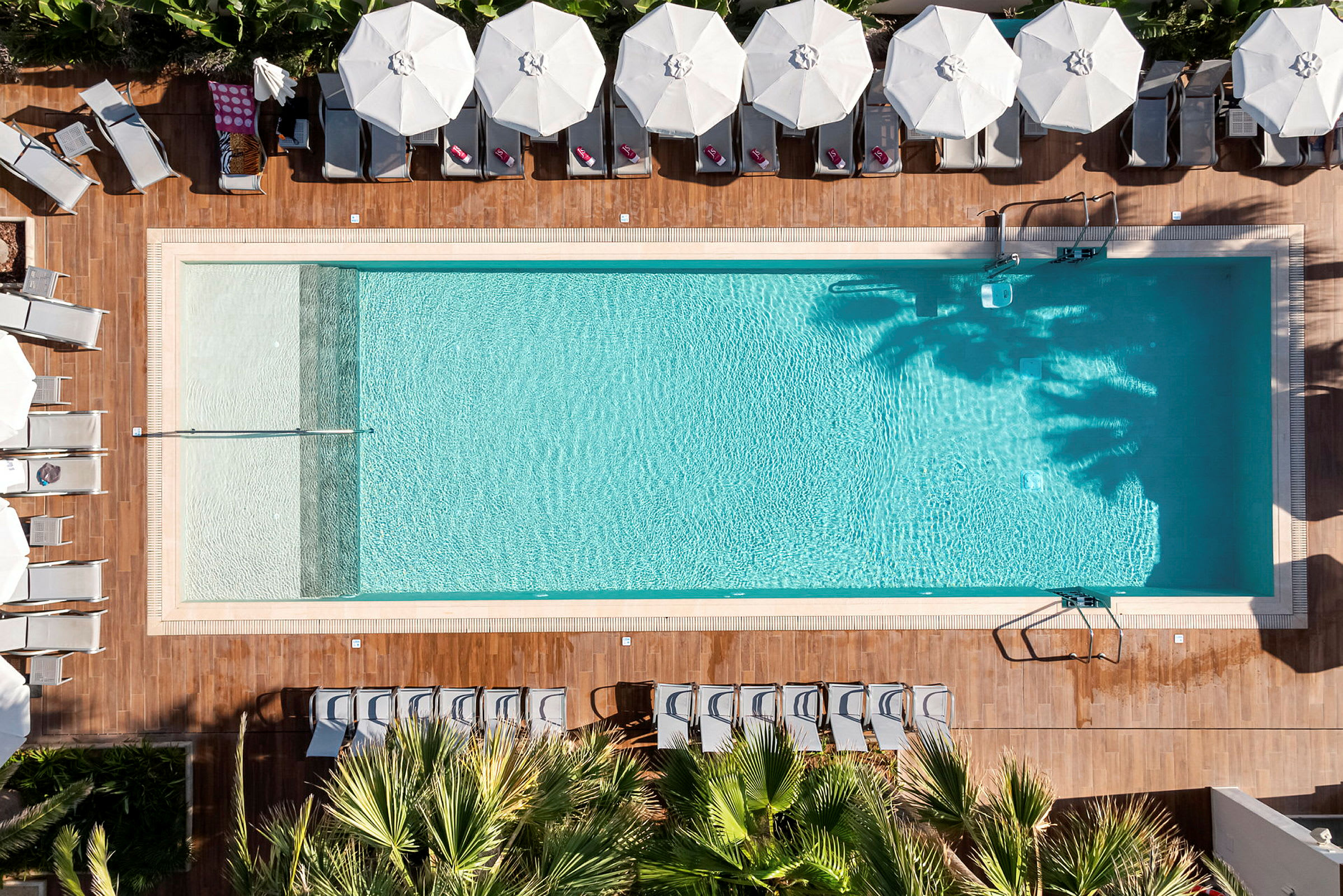 Luftbild av en rektangulär swimmingpool omgiven av solstolar och parasoller. (AI-genererad text)