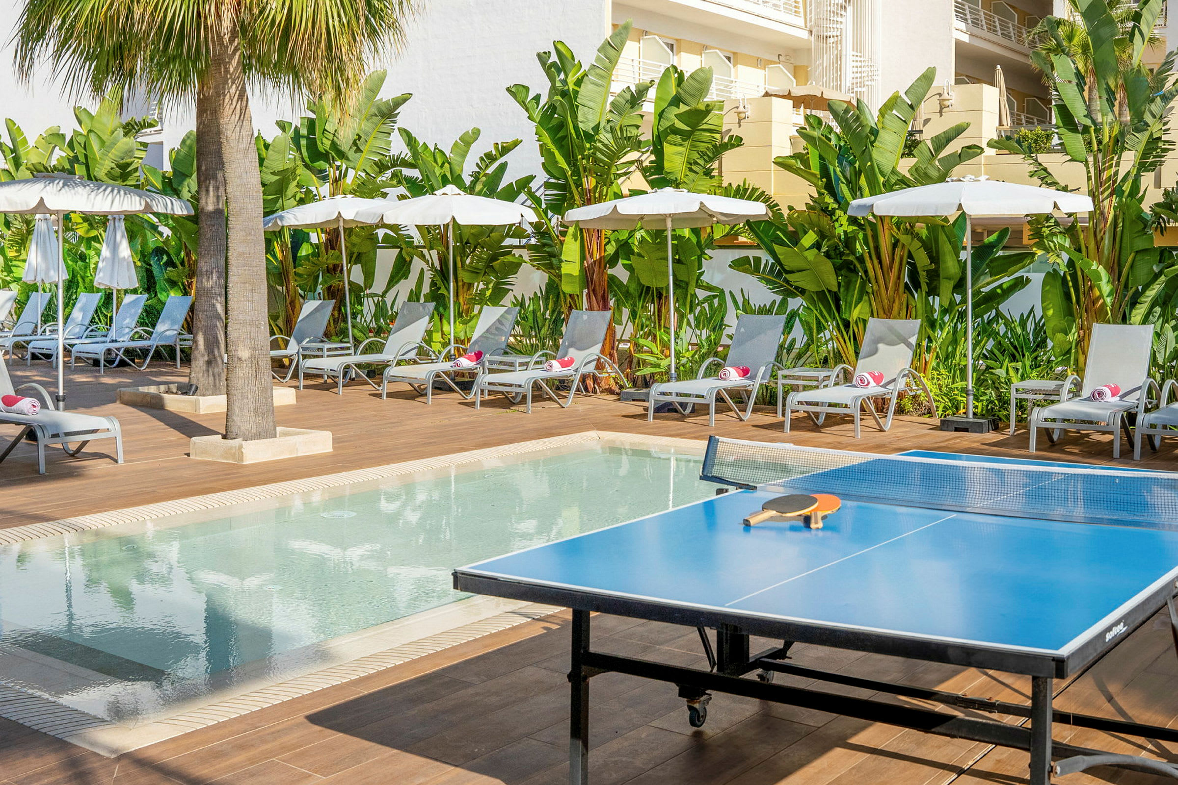 En bordtennisbord vid en pool med solstolar och parasoller. (AI-genererad text)