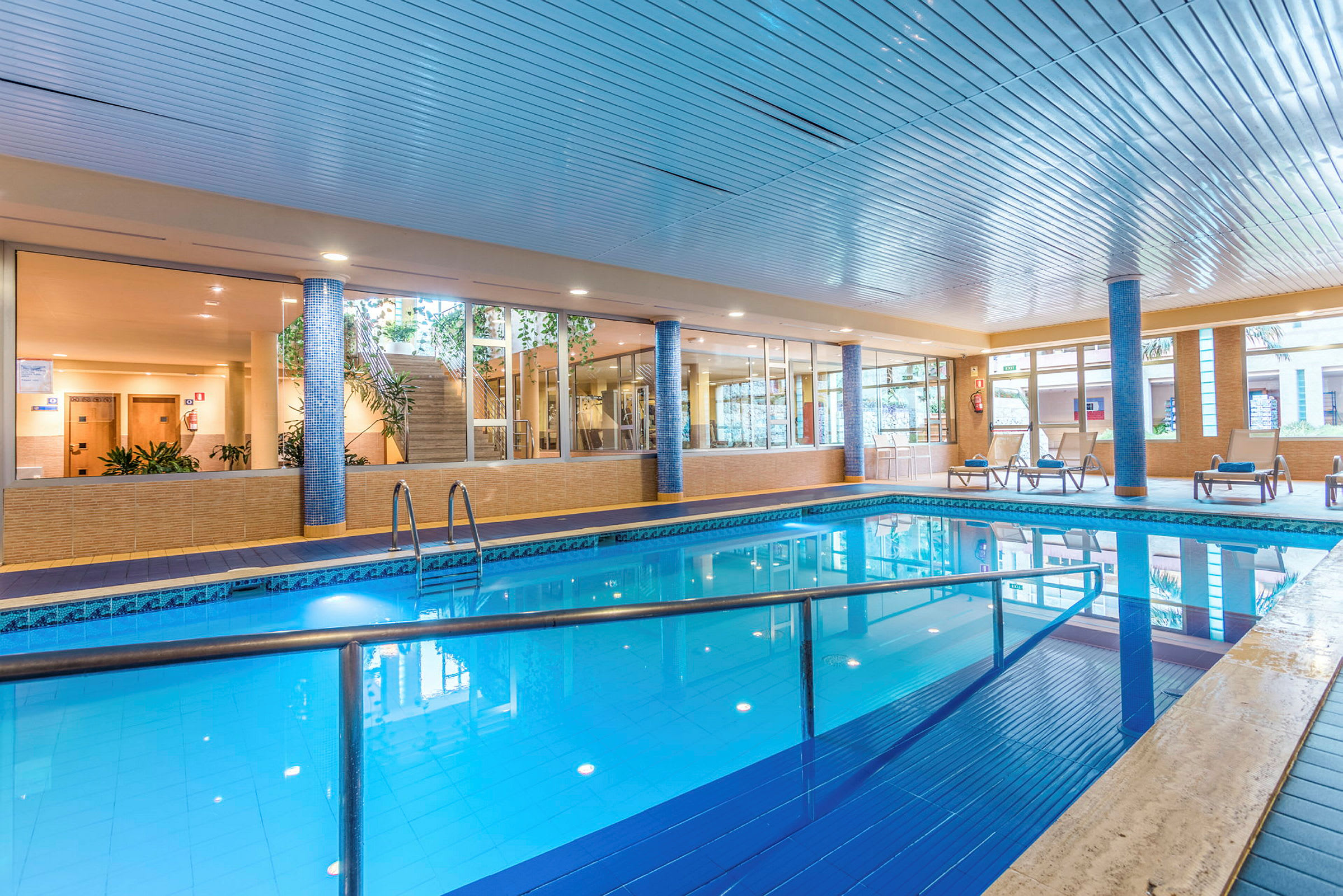 Inomhuspool med solstolar och omgivande glasväggar. (AI-genererad text)