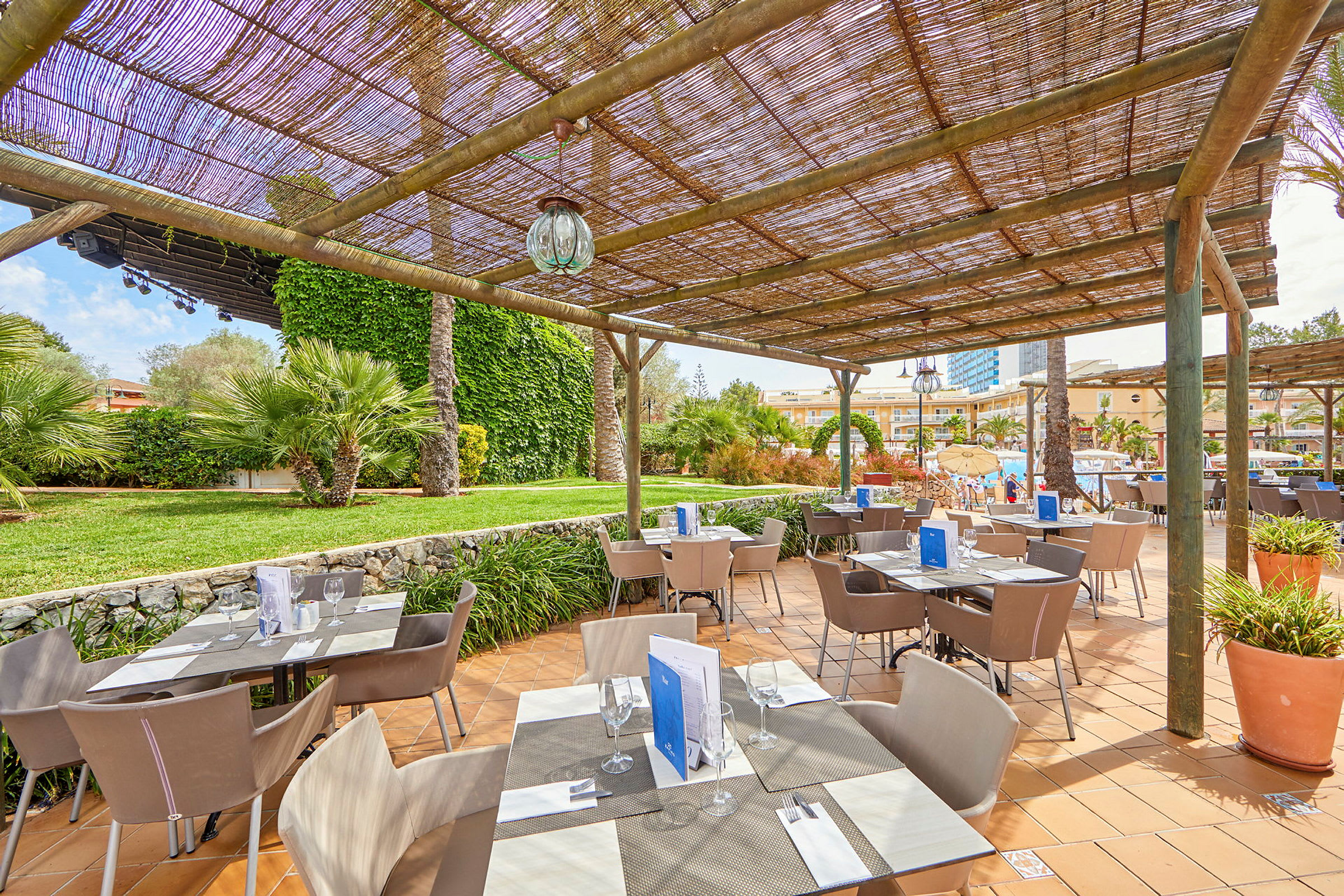 En utomhusrestaurang med solskydd i en grönskande trädgårdsmiljö. (AI-genererad text)