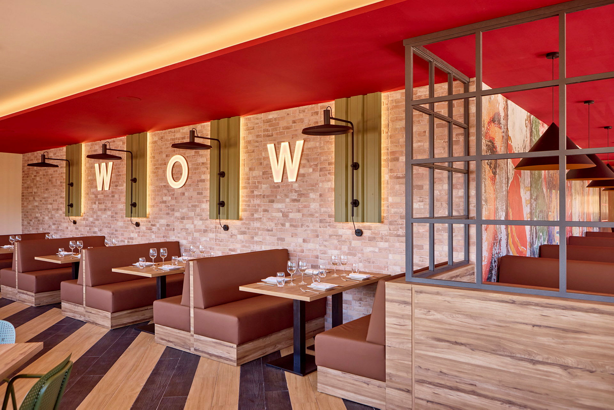 Restaurangmiljö med bruna sittplatser, träbord och tegelvägg dekorerad med bokstaven "WOW". (AI-genererad text)