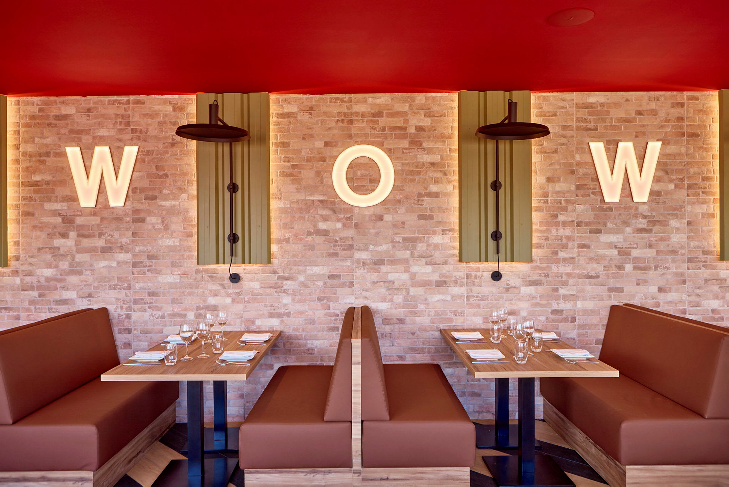 Två sittplatser med bord och soffor i en restaurang, med belysta bokstäver "W" och "O" på en tegelvägg. (AI-genererad text)