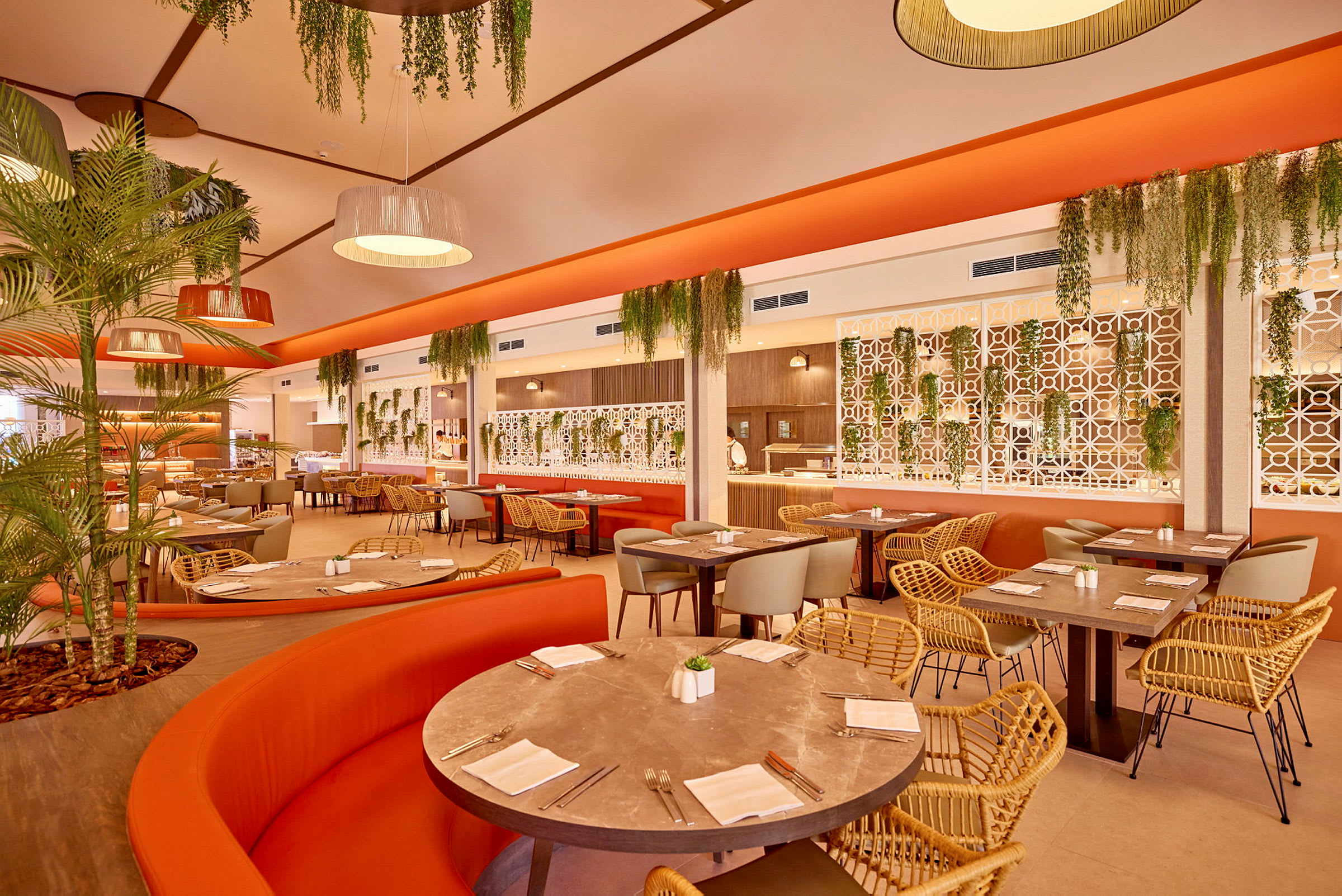 En restaurang med orangea soffor, flätade stolar och gröna växter. (AI-genererad text)