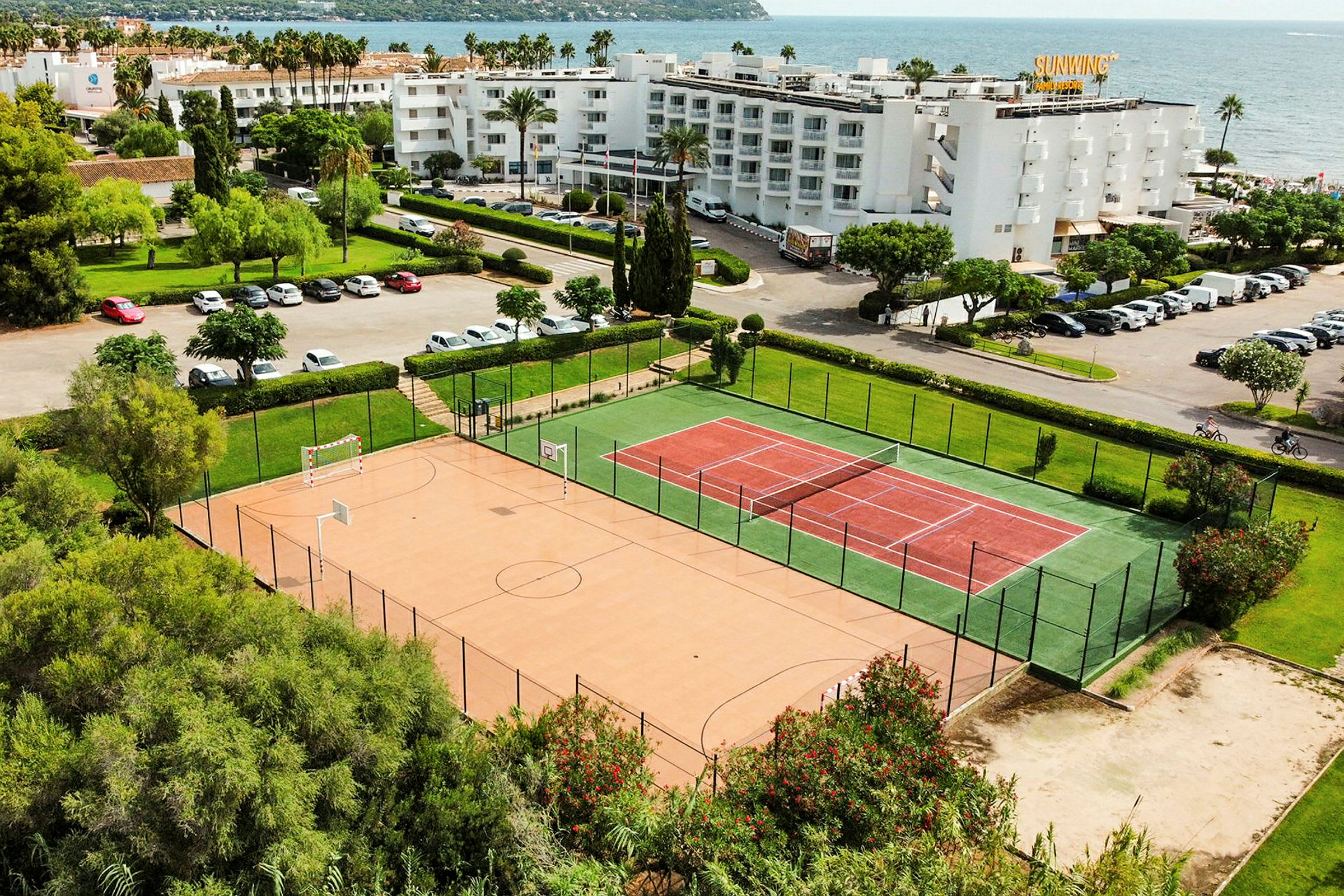 Bild av ett tennis- och sportområde nära havet, med byggnader och parkeringsplatser i bakgrunden. (AI-genererad text)