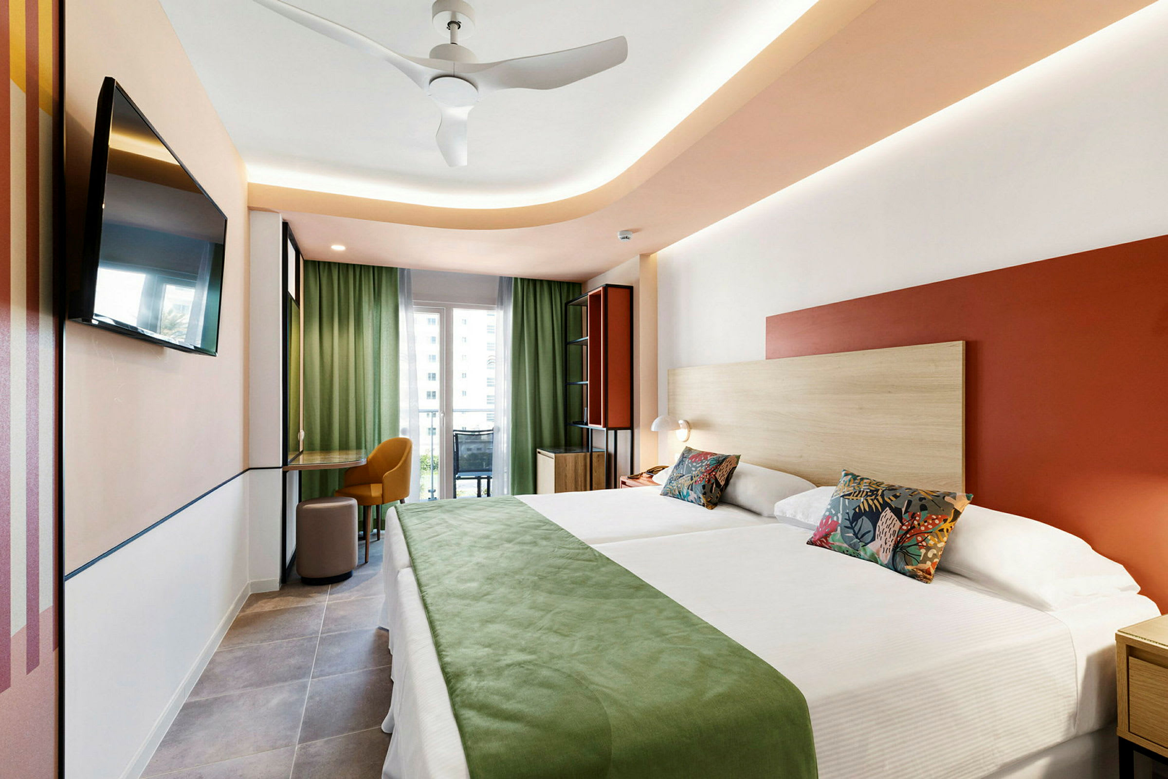 Ett modernt hotellrum med två sängar, grön inredning och en balkong med utsikt. (AI-genererad text)