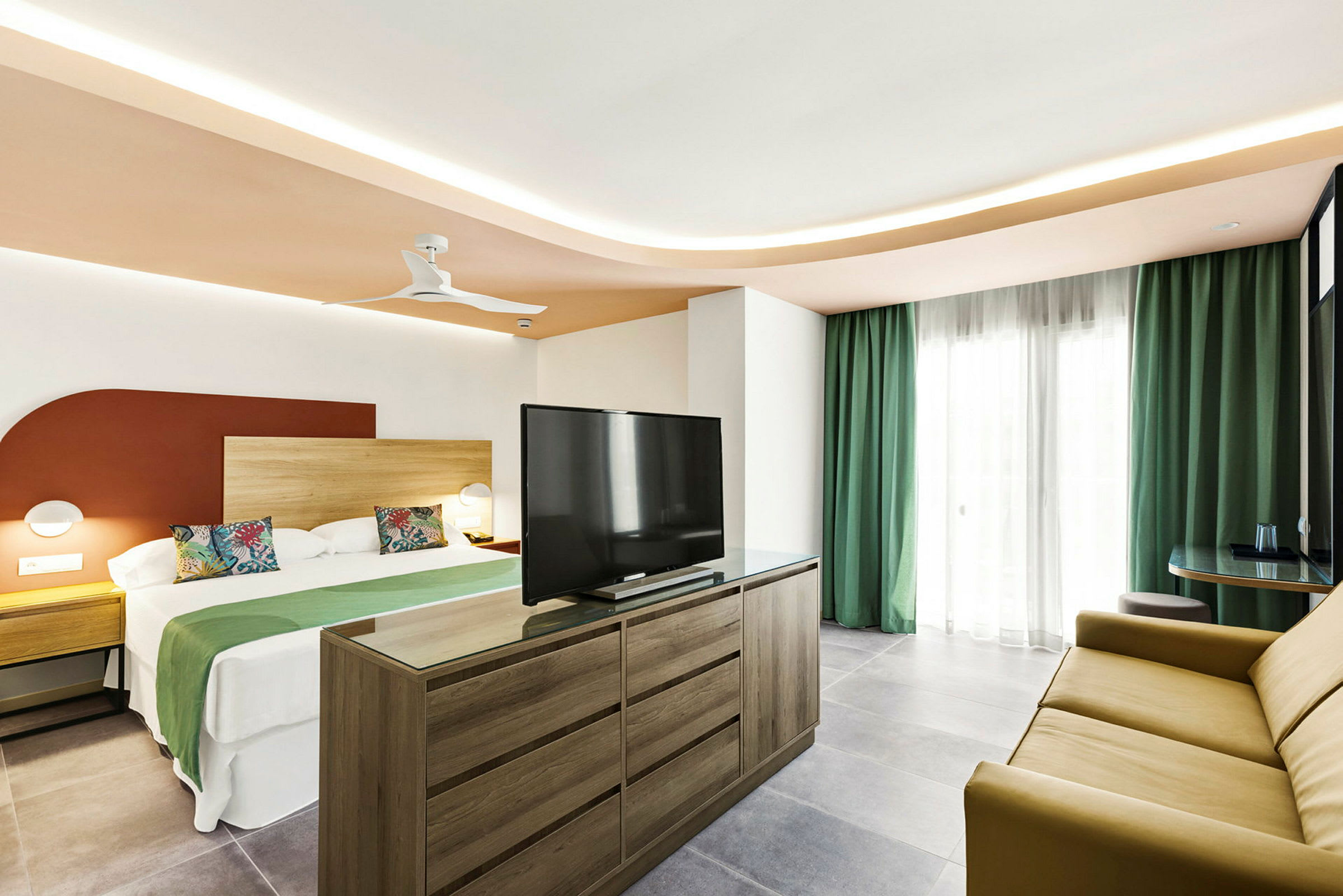 Ett hotellrum med en stor säng, en byrå med TV, och en soffa samt gardiner framför fönstret. (AI-genererad text)