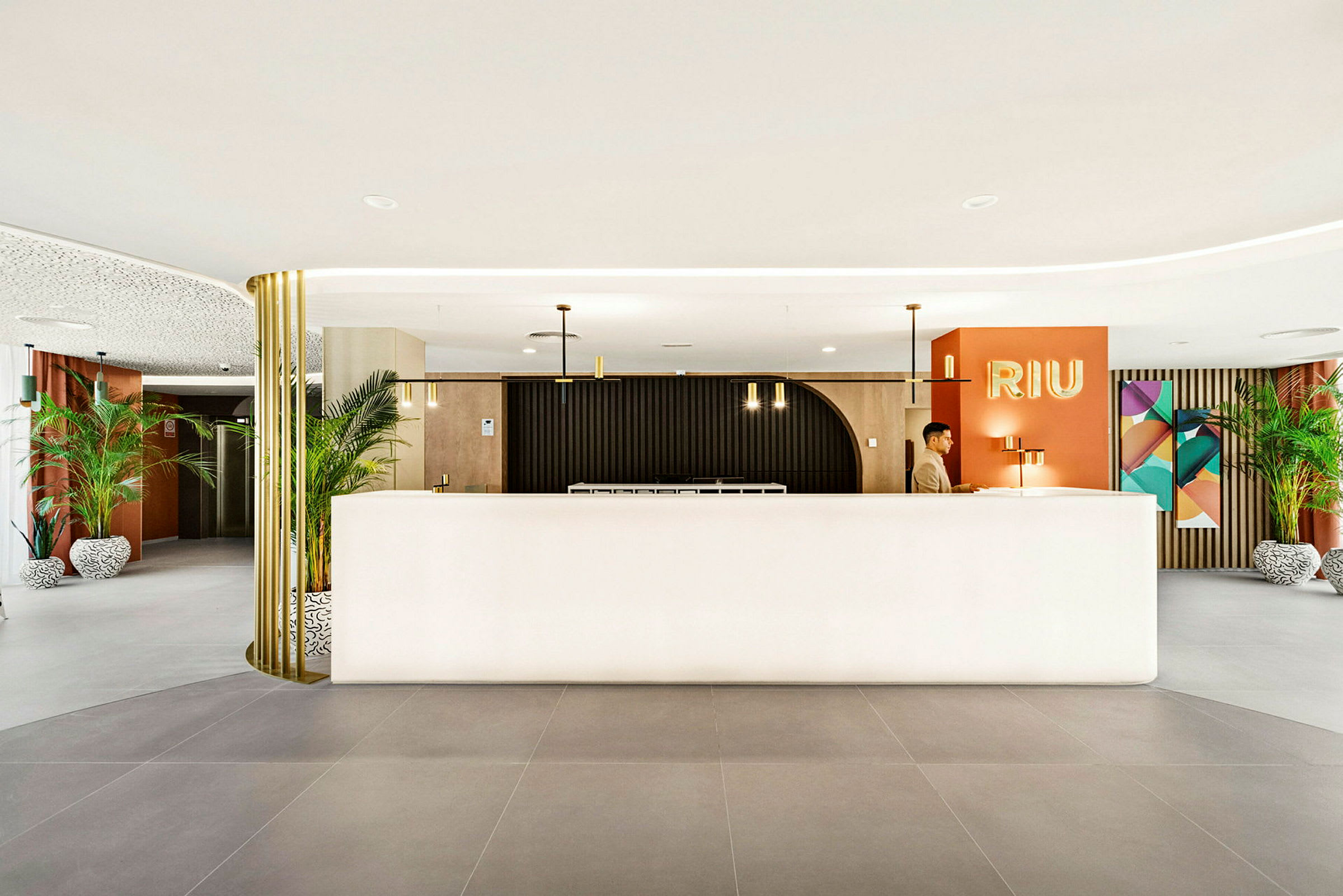 Receptionen på ett hotell med en modern inredning, där växter, lampor och dekorationer omger en ljus receptionsdisk.  (AI-genererad text)