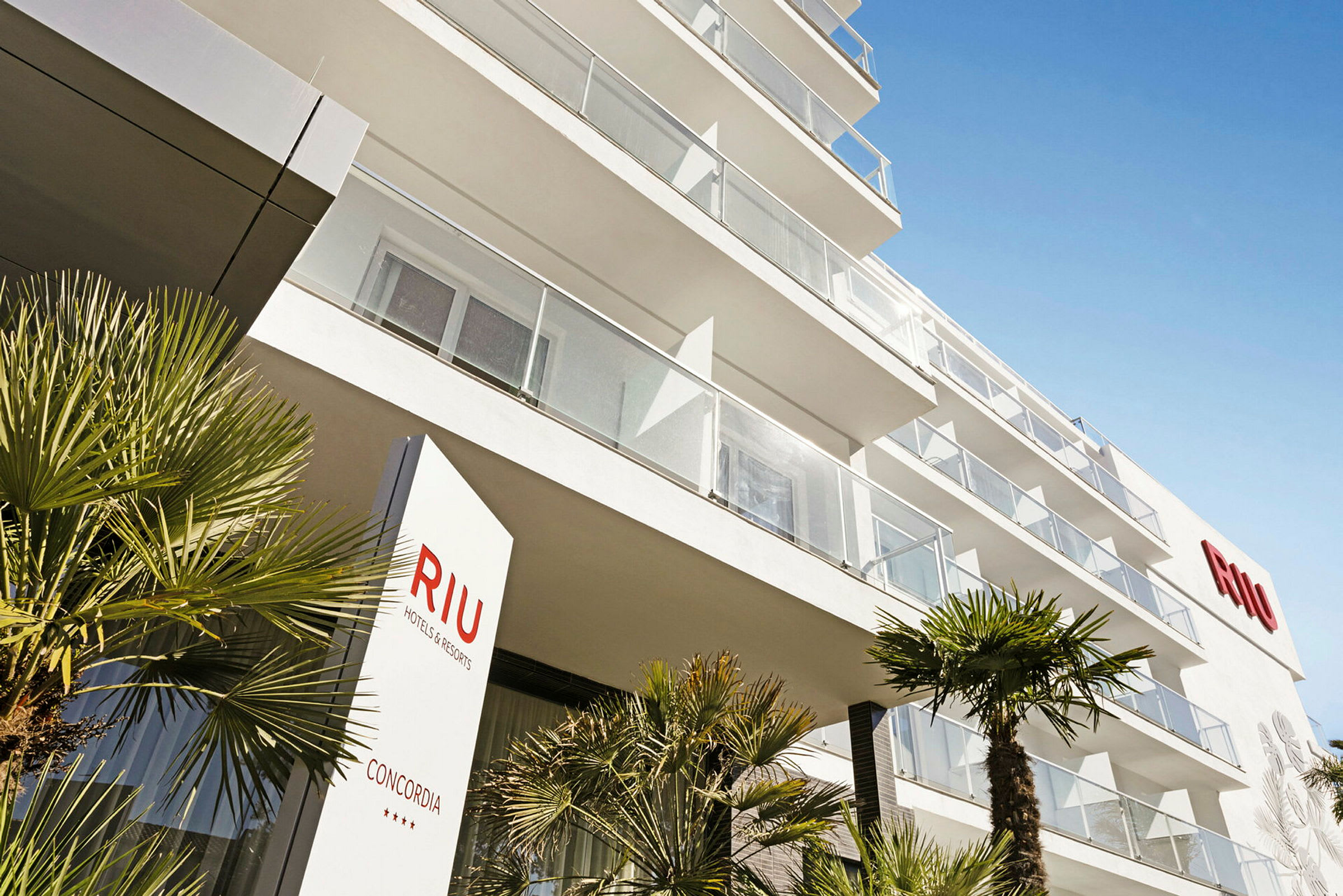 En modern hotellbyggnad med balkonger och palmer i förgrunden. (AI-genererad text)