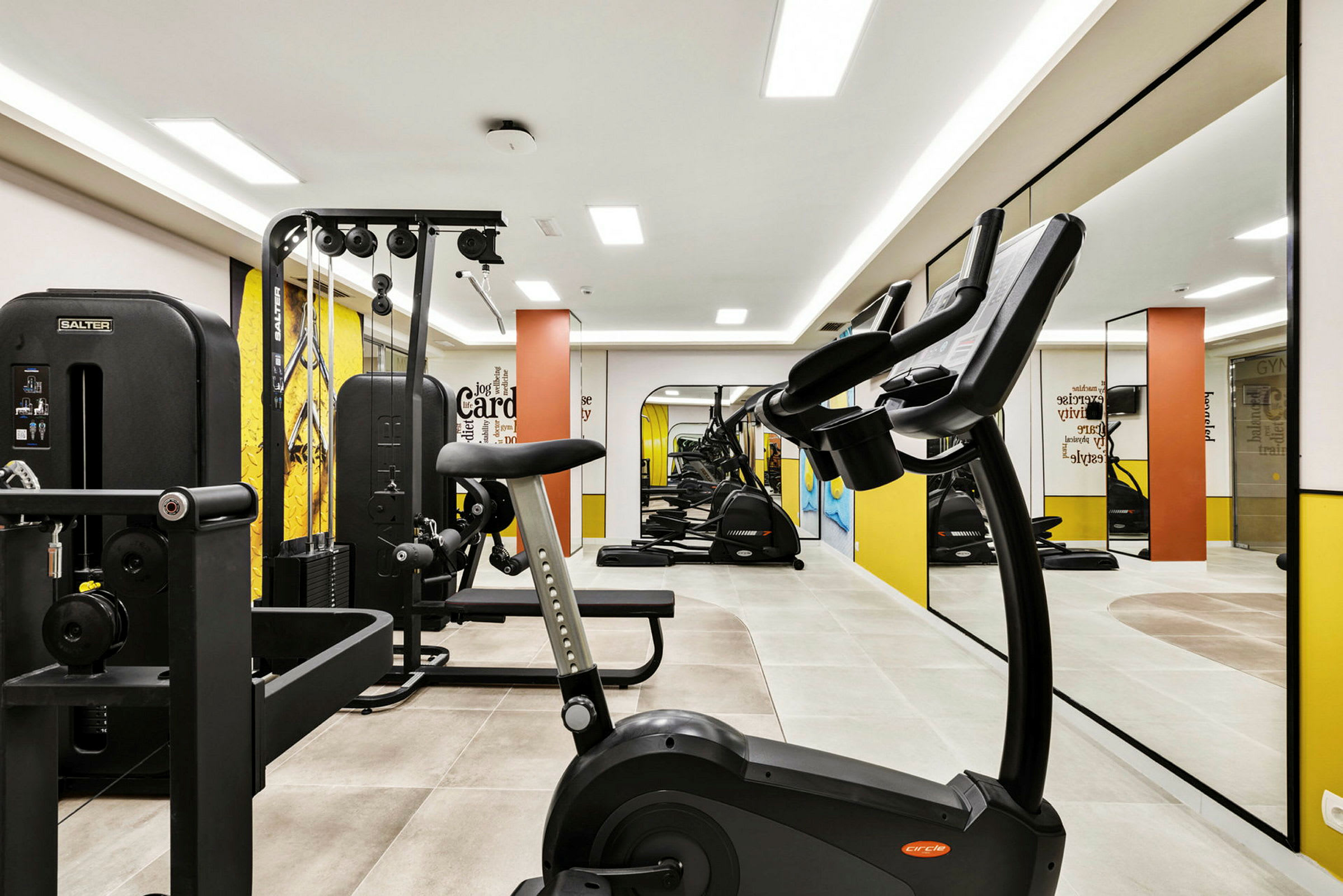 Ett gym med träningsutrustning såsom motionscyklar, styrketräningsmaskiner och speglar på väggen. (AI-genererad text)