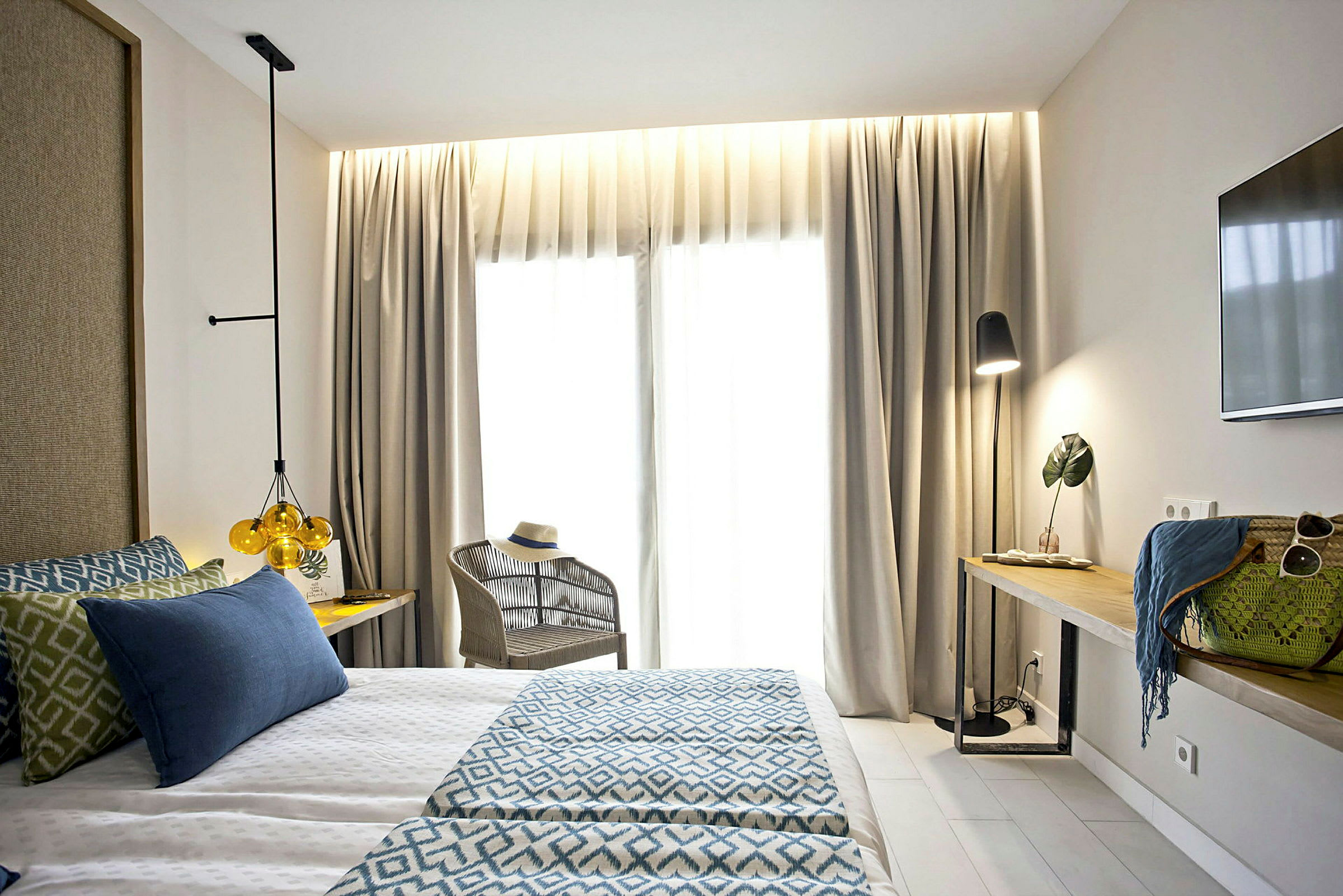 Ett ljust hotellrum med en dubbelsäng, fåtölj och ett bord med dekorativa föremål och lampa. (AI-genererad text)