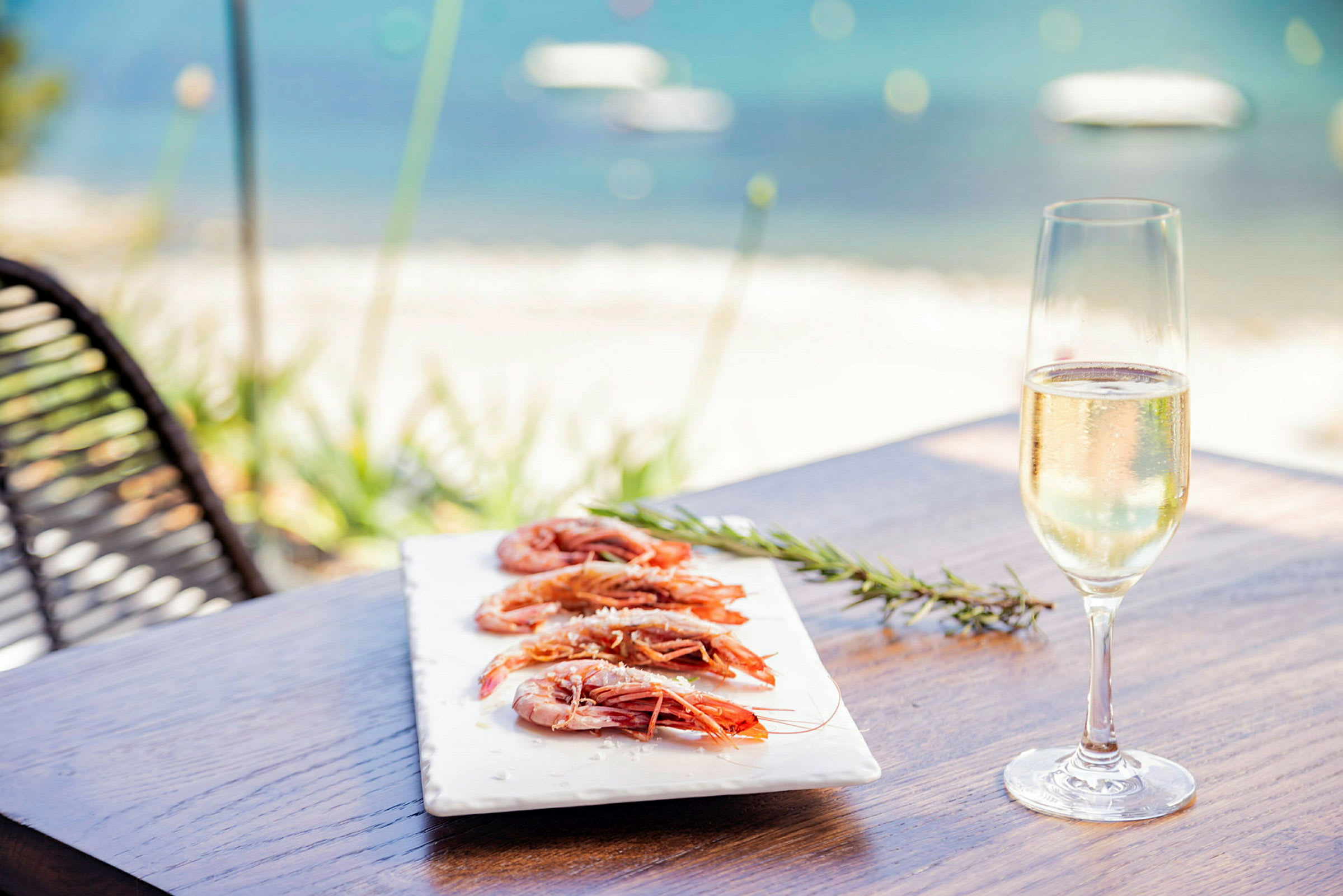 En tallrik med räkor och ett glas champagne på ett bord vid havet. (AI-genererad text)