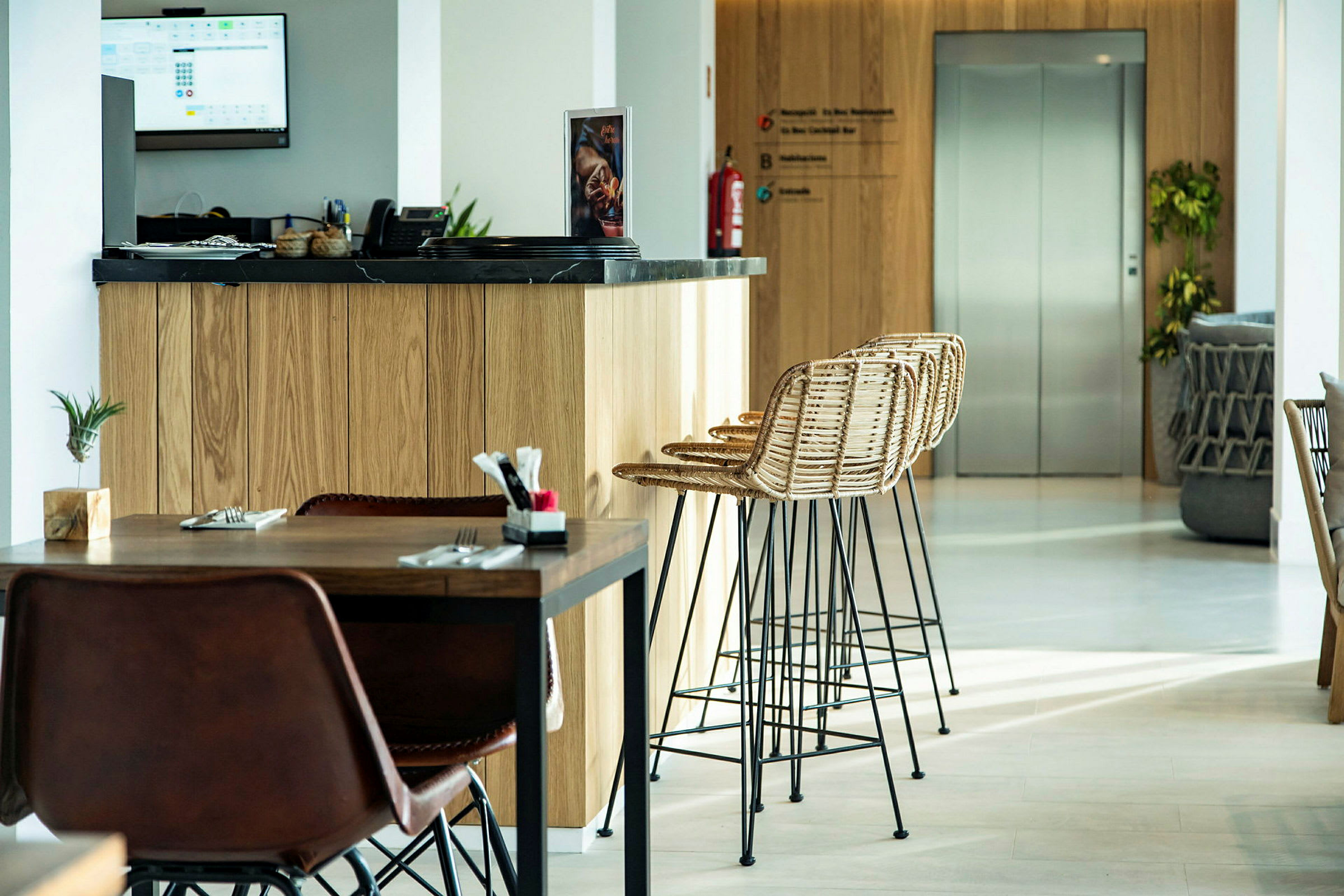 En modern lobby med en träinredd receptionsdisk och sittplatser, samt en hiss i bakgrunden. (AI-genererad text)