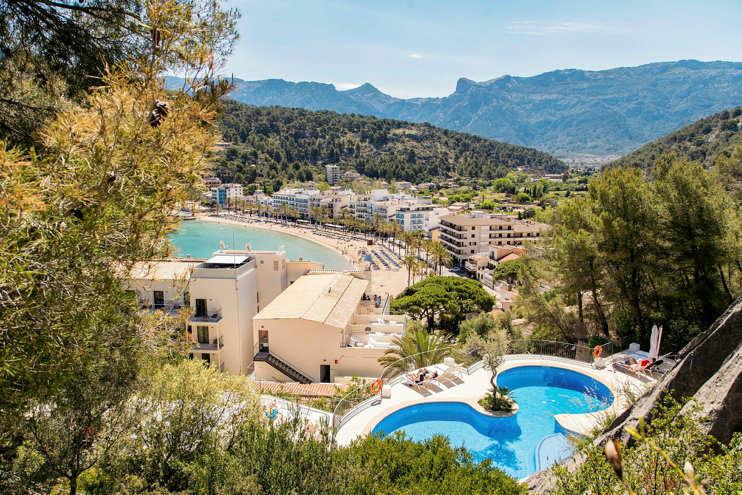 Utsikt över en strandstad med hotell, pool och berg i bakgrunden. (AI-genererad text)