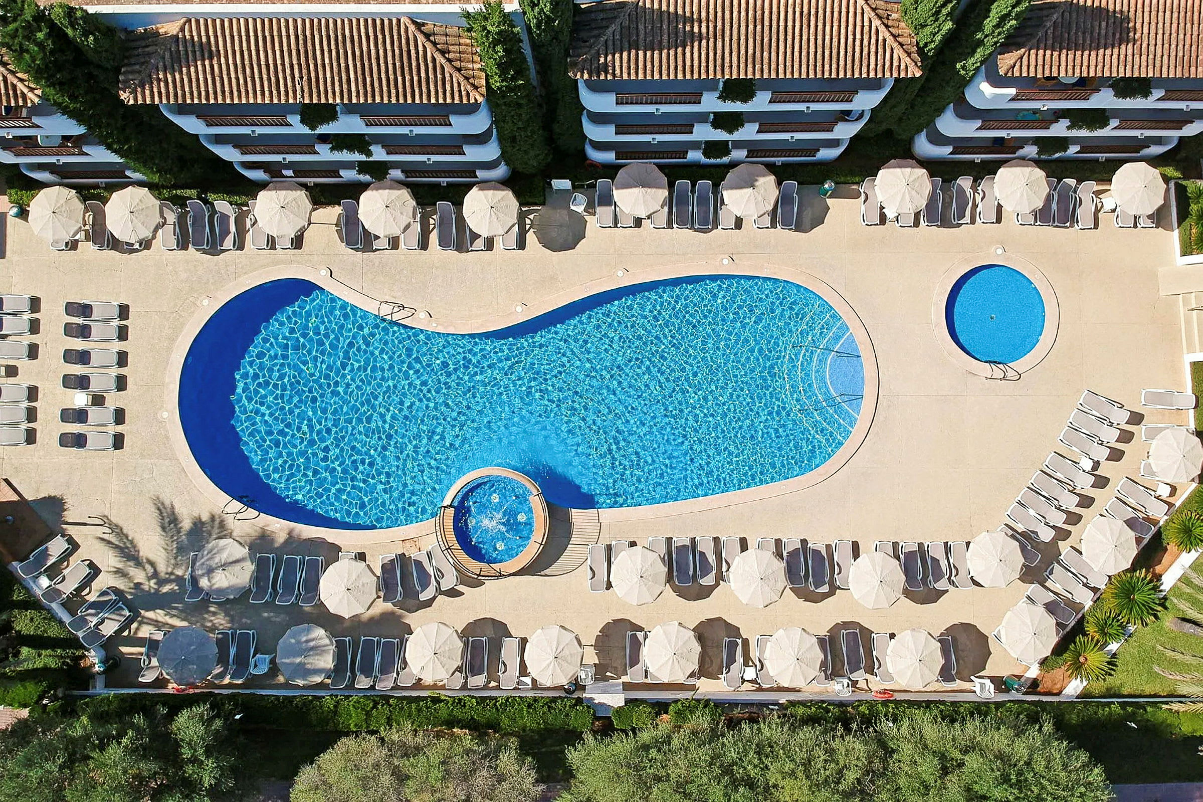Flygfotografi av en swimmingpool med solstolar och parasoller runtom. (AI-genererad text)