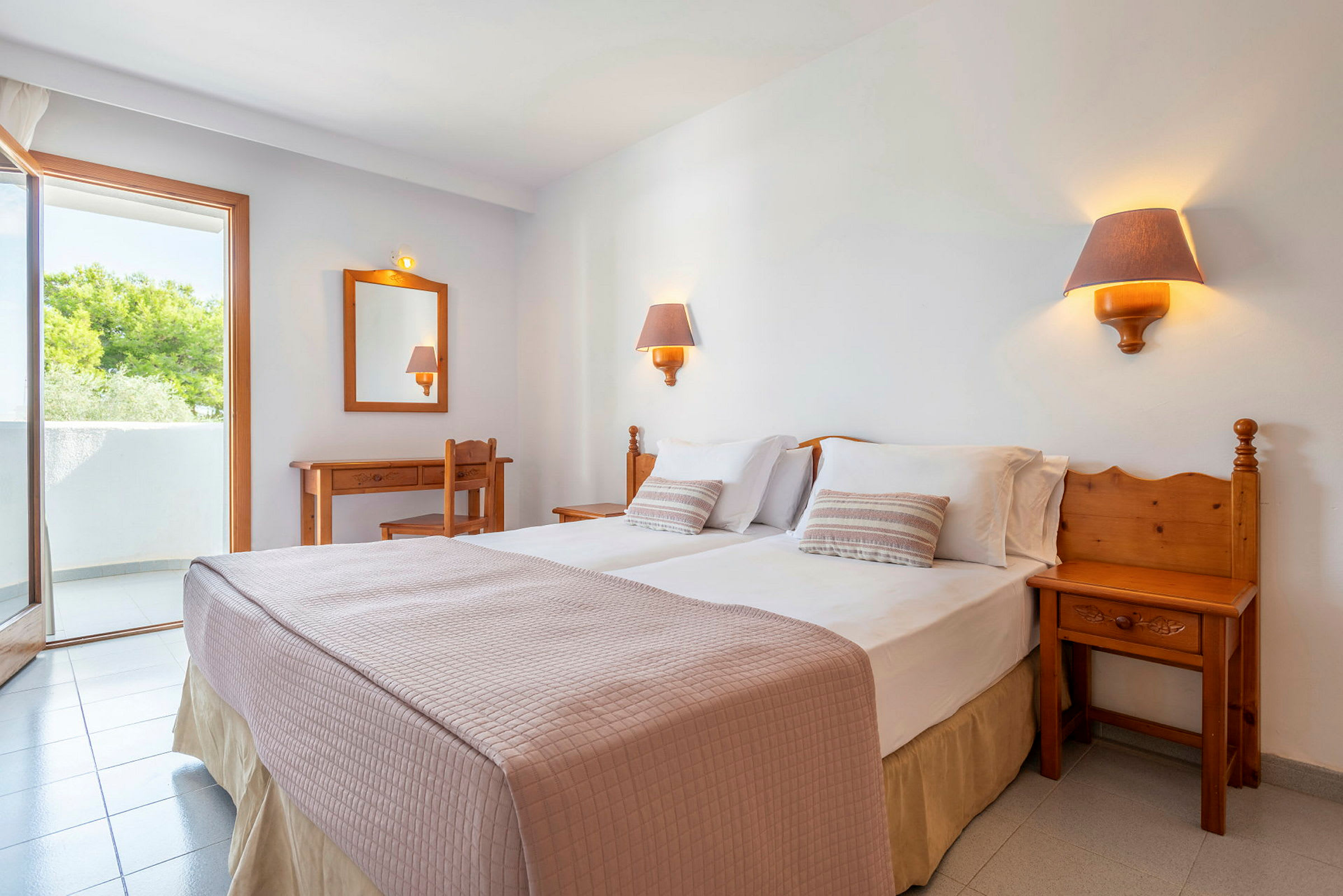 Ett hotellrum med en dubbelsäng, två sänglampor, ett skrivbord, en stol och en balkong. (AI-genererad text)