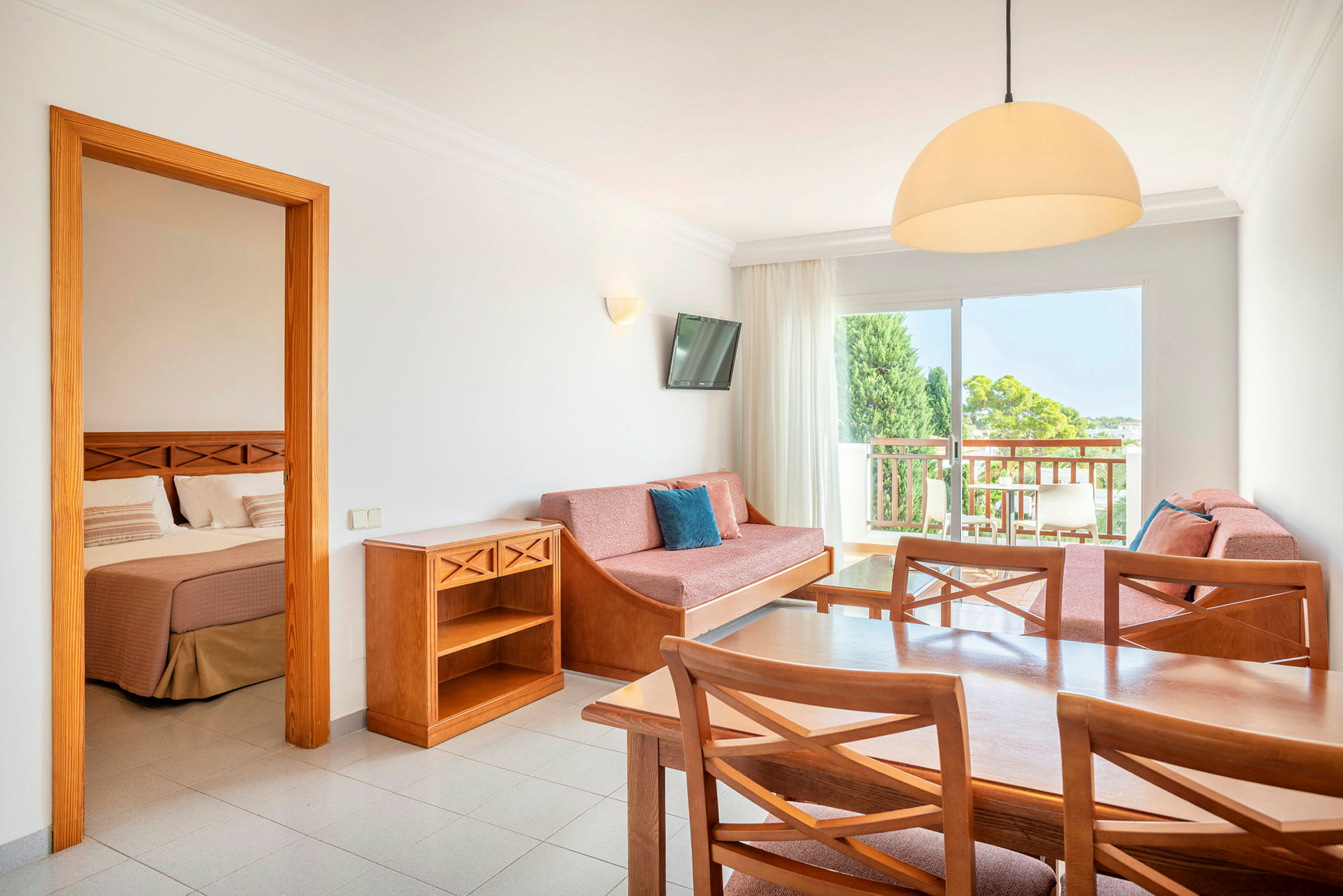 En hotellrumsvit med ett bord, stolar, soffa och ett sovrum synligt genom en öppen dörr. (AI-genererad text)