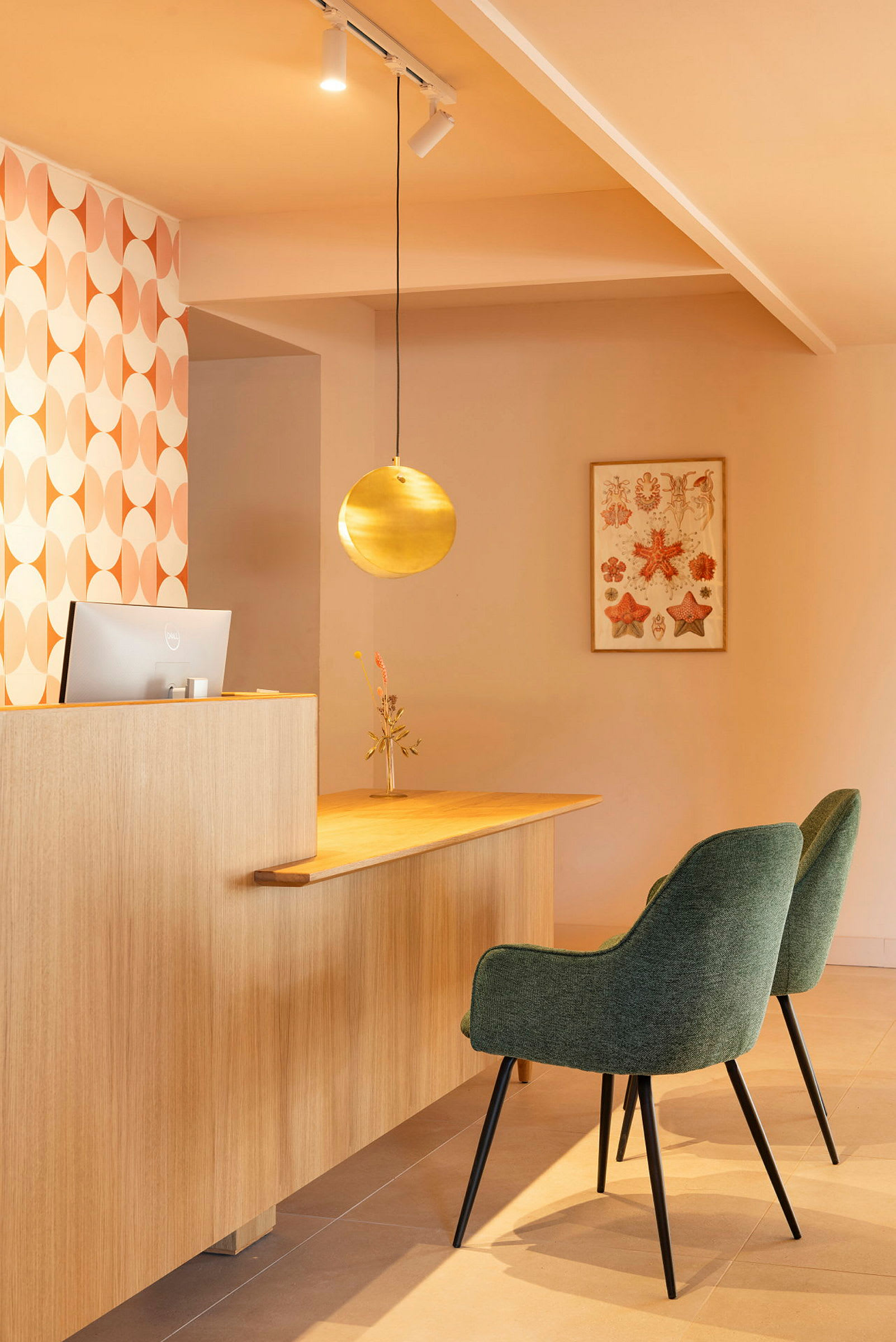 Bild på en receptionsdisk med två gröna stolar, en metallisk rund lampa och väggdekoration. (AI-genererad text)