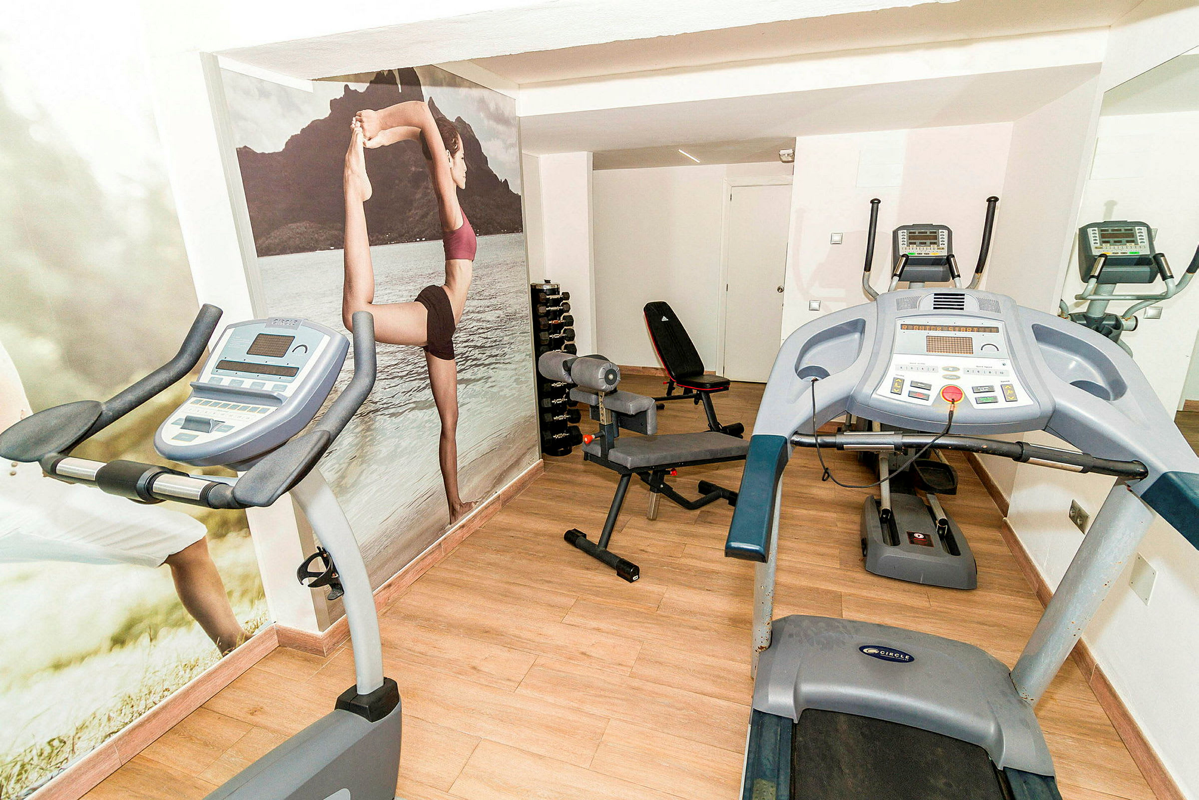 Ett gym med träningsutrustning, inklusive löpband och träningscykel. Väggarna har motiv av människor som tränar. (AI-genererad text)