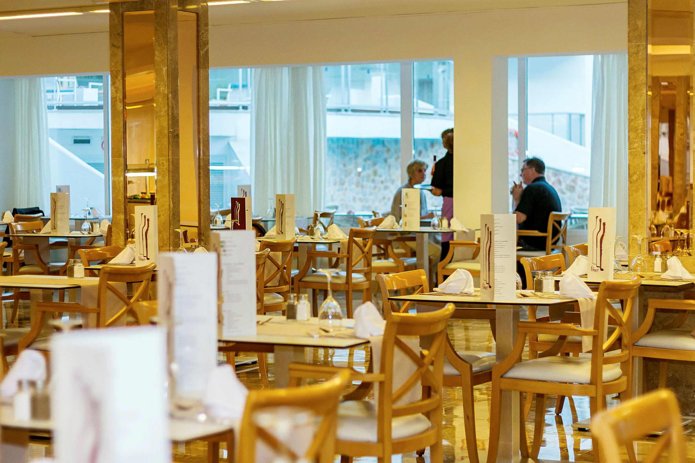 Restaurang med dukade bord och trästolar, fönster i bakgrunden. (AI-genererad text)